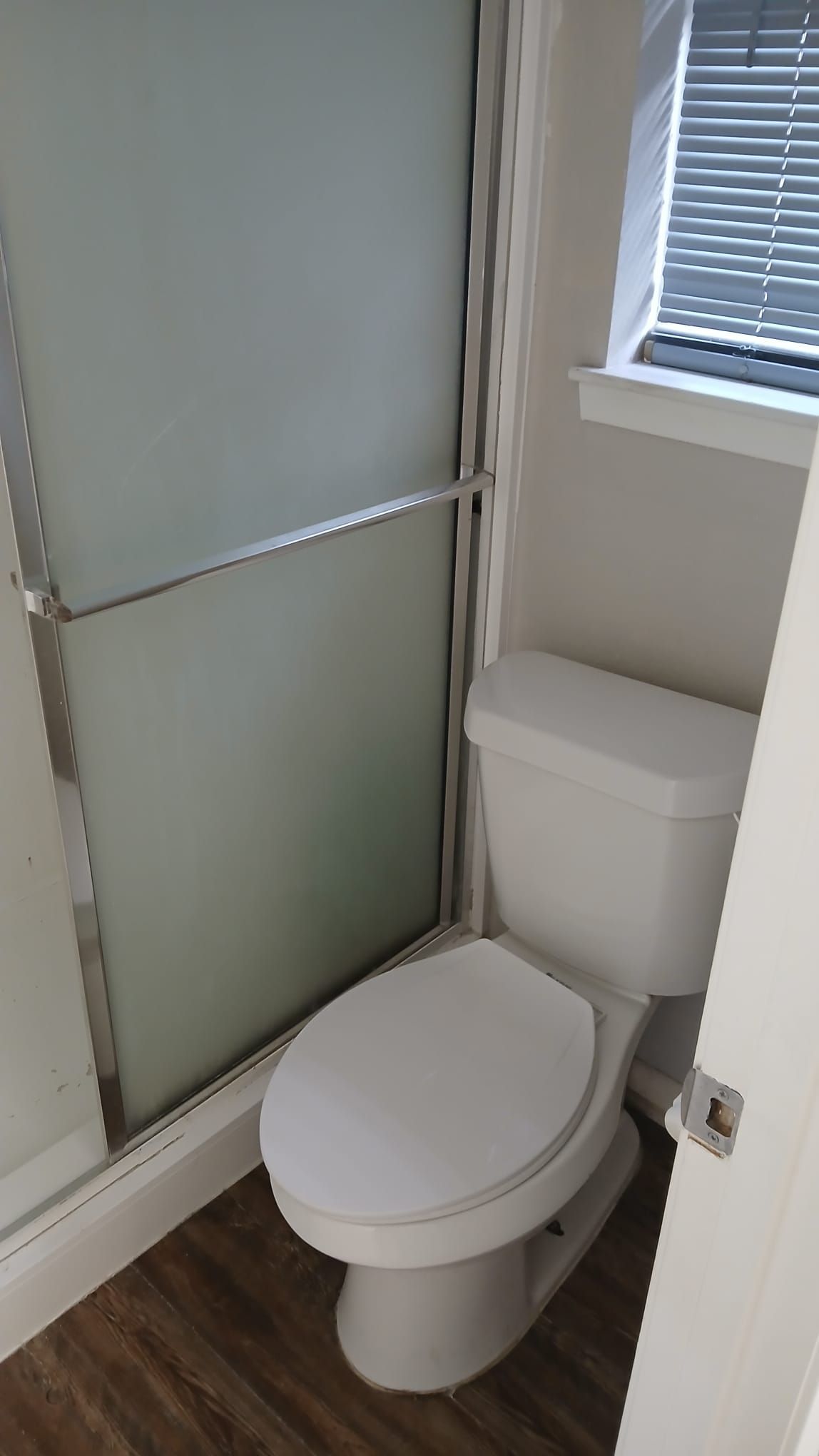 Bathroom with white toilet, frosted shower door, and window with blinds.