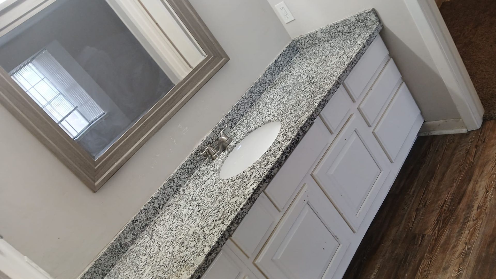 White bathroom vanity with gray granite countertop, oval sink, and framed mirror.