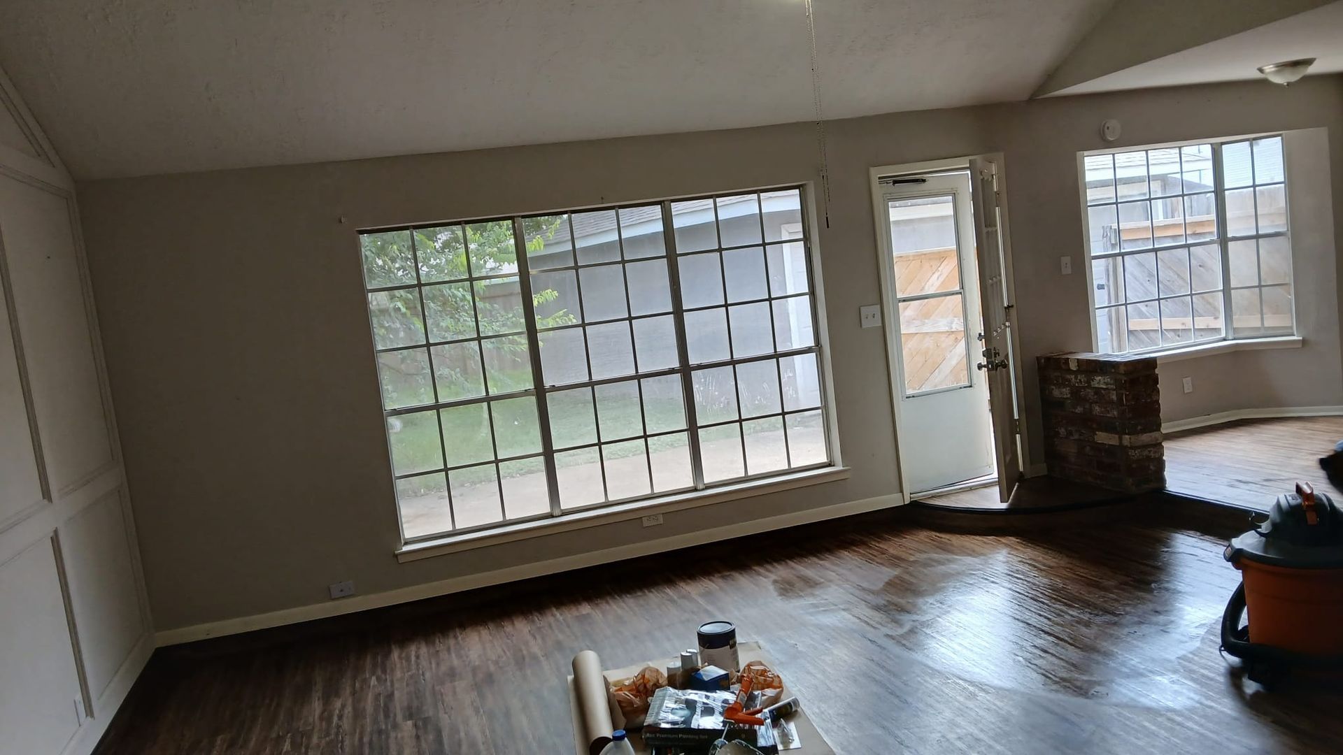 Room with large windows and door, dark wood floor, light gray walls, and partially installed trim.