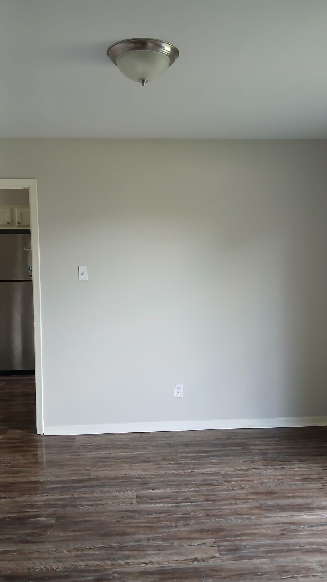 Room with gray walls, wood-look floor, light fixture on ceiling, and doorway to kitchen.