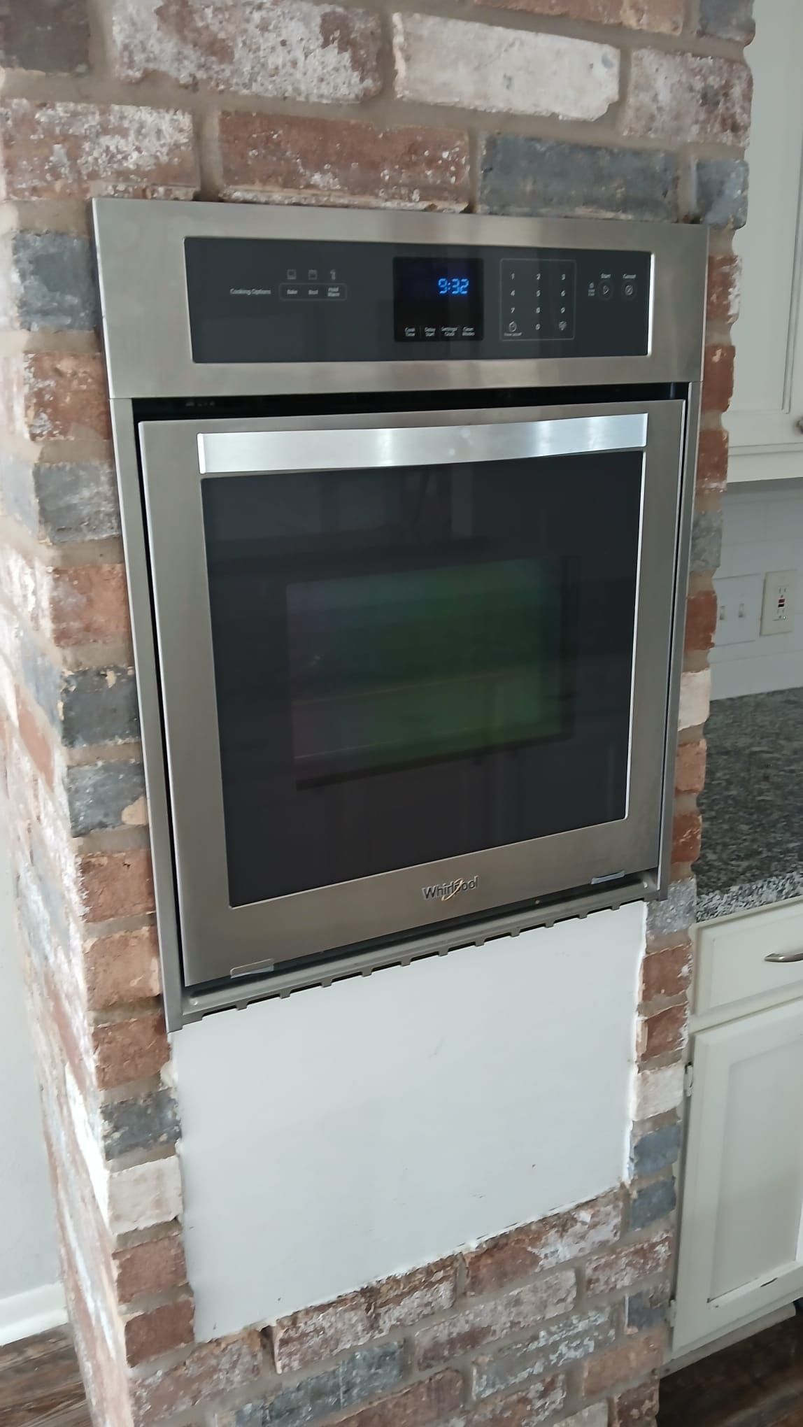 Stainless steel oven built into a brick wall. The oven door is closed, with a digital display above.