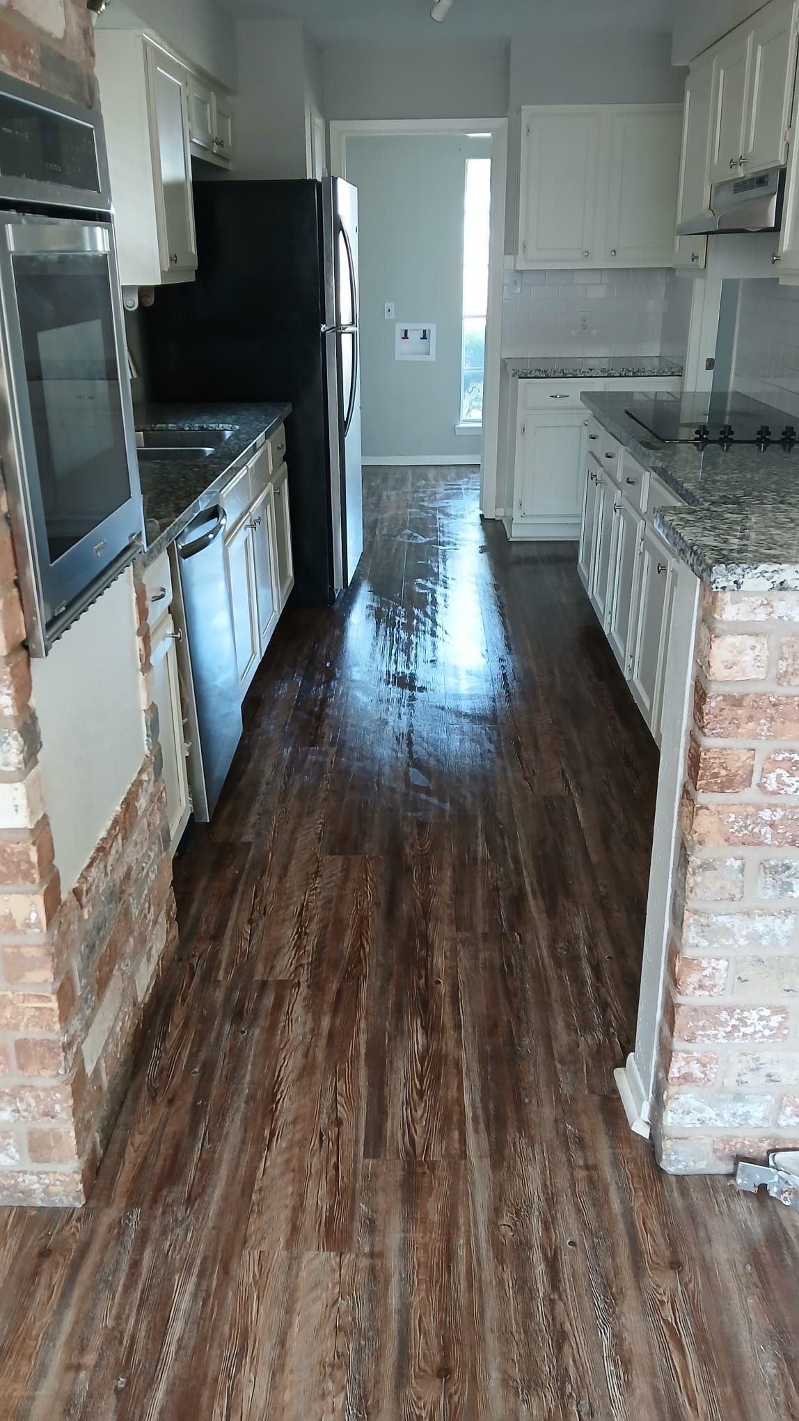 Kitchen with wooden floor, white cabinets, and dark refrigerator.