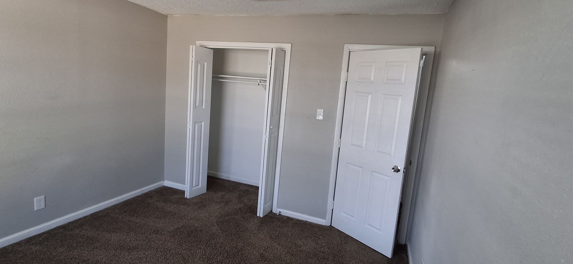 Empty room with a closet and a closed door. Gray walls and brown carpet.