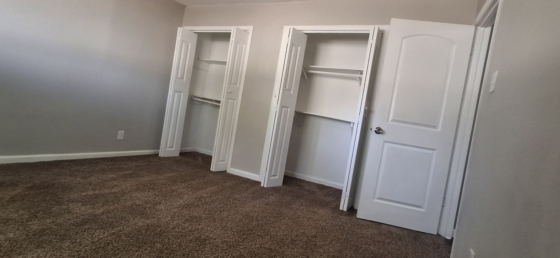 Room with brown carpet, gray walls, two white closet openings, and a closed white door.