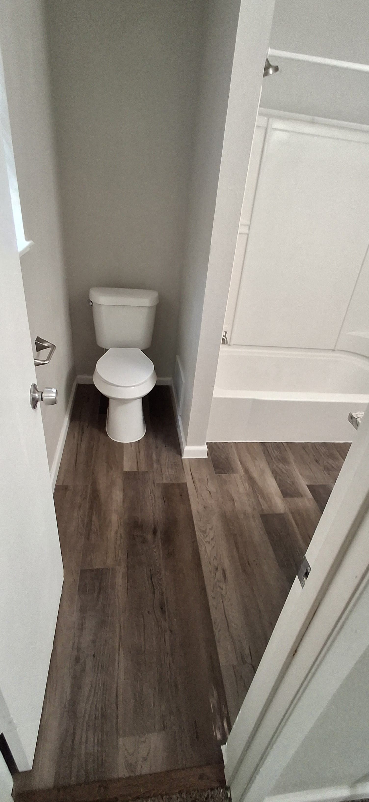 Bathroom with a toilet, gray walls, and wood-look flooring. A shower is to the right.