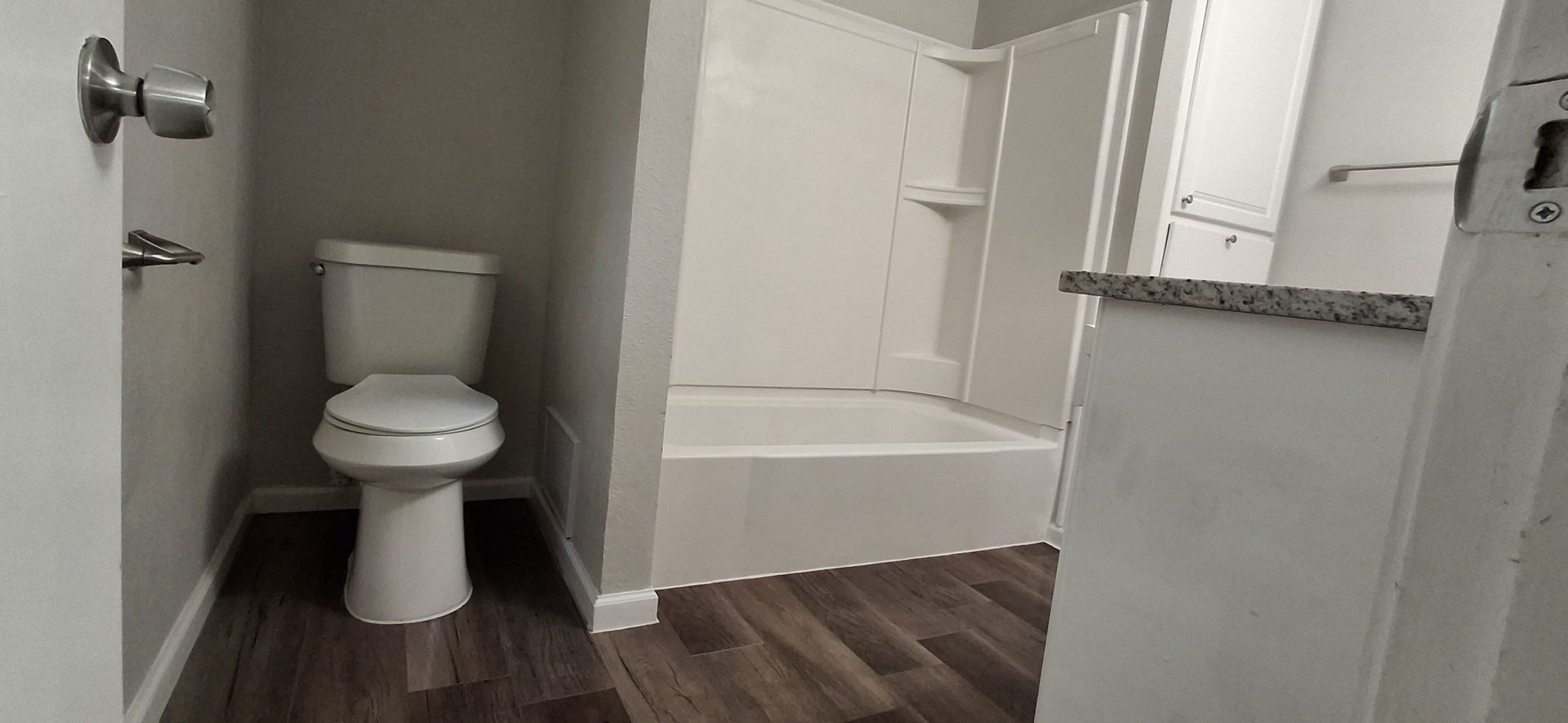 Bathroom interior with a white toilet, shower/tub, and dark wood-look floor.
