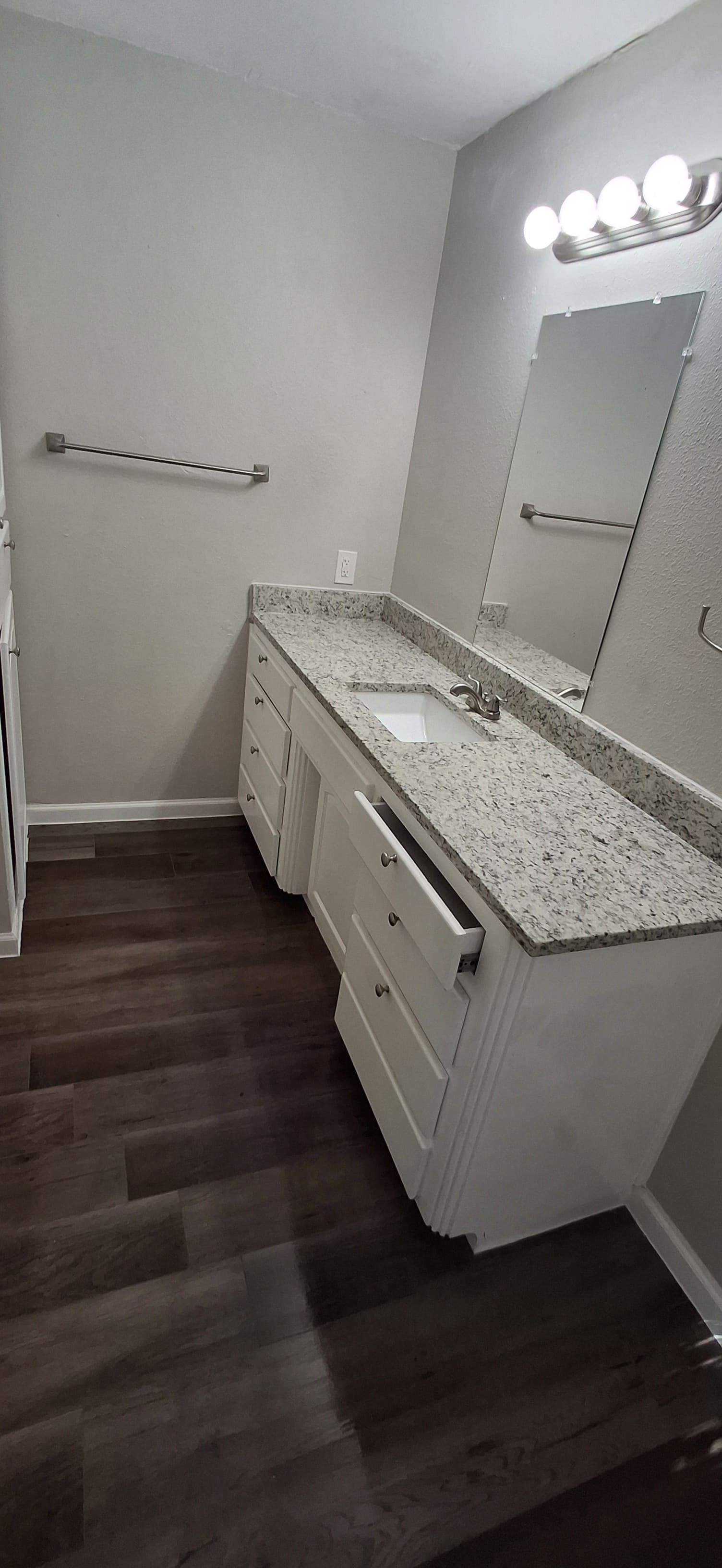 Bathroom with white cabinets, granite countertop, and dark wood-look flooring. A mirror and light fixture are above the sink.