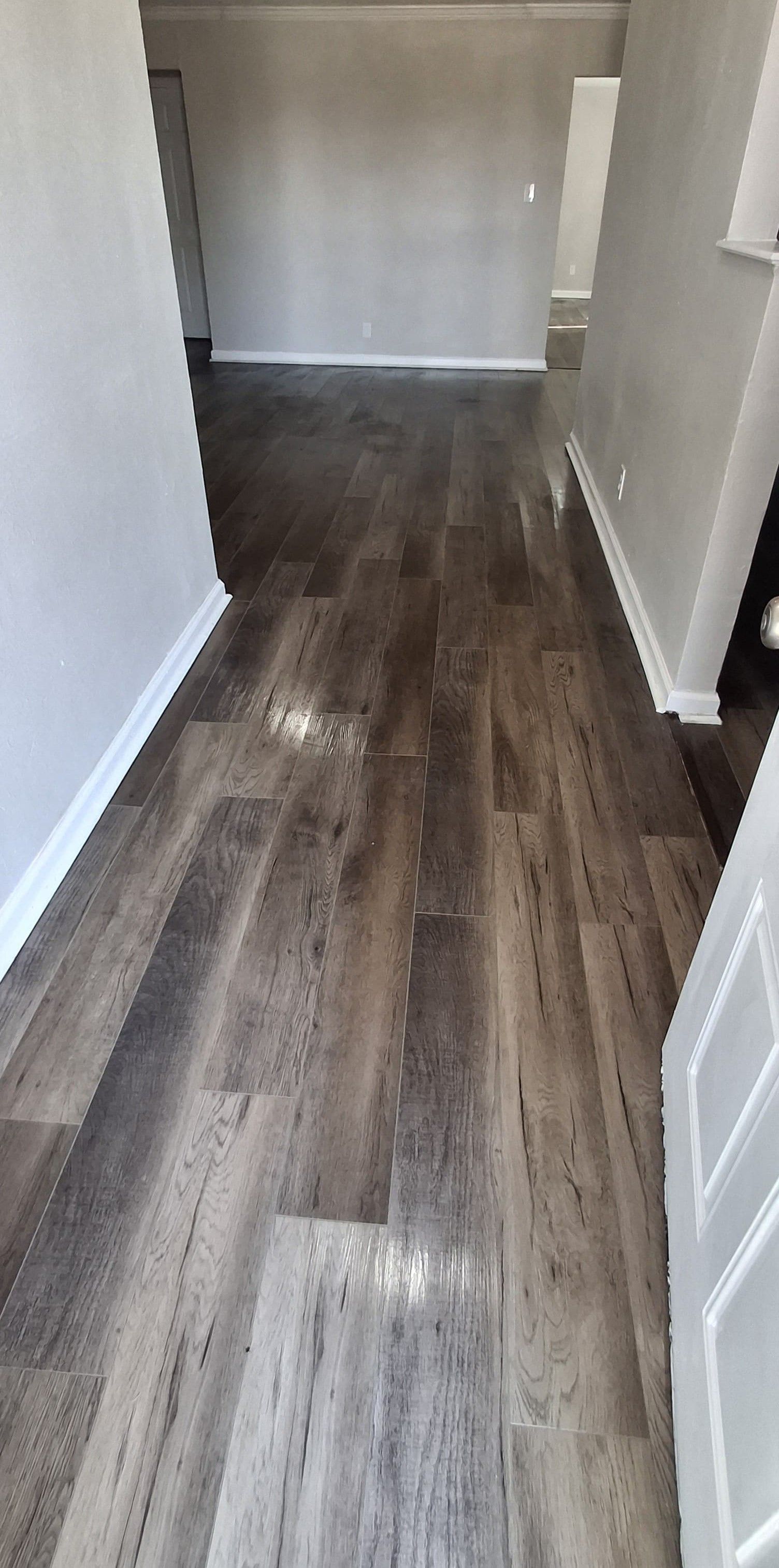 Wooden floorboards leading down a hallway with white trim and gray walls.