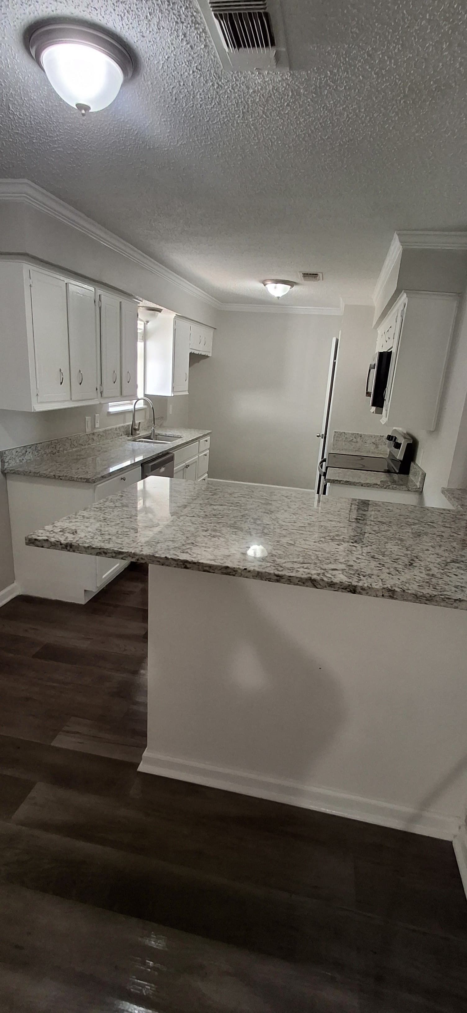 Kitchen with white cabinets, granite countertops, and dark wood flooring.