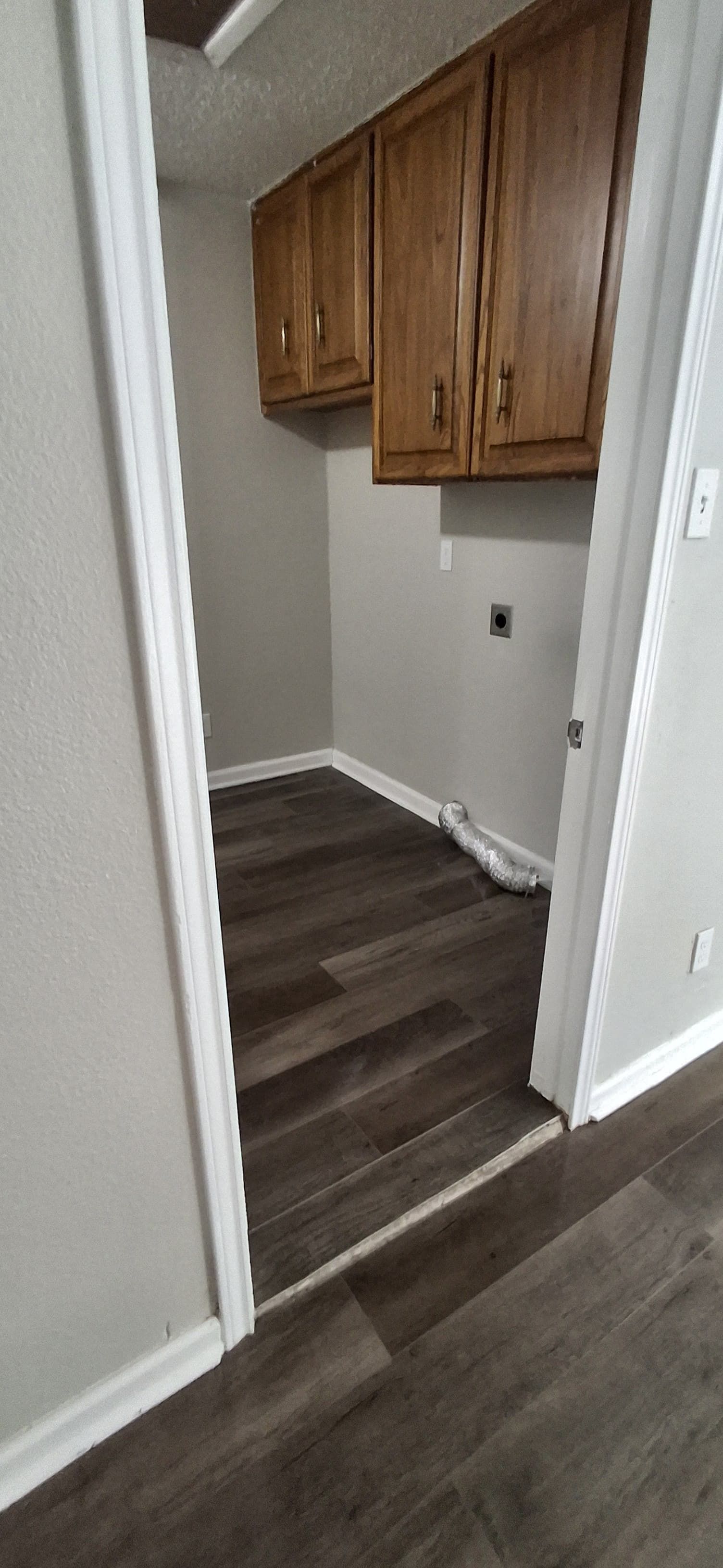 View into a laundry room with brown cabinets, gray walls, and dark wood flooring.