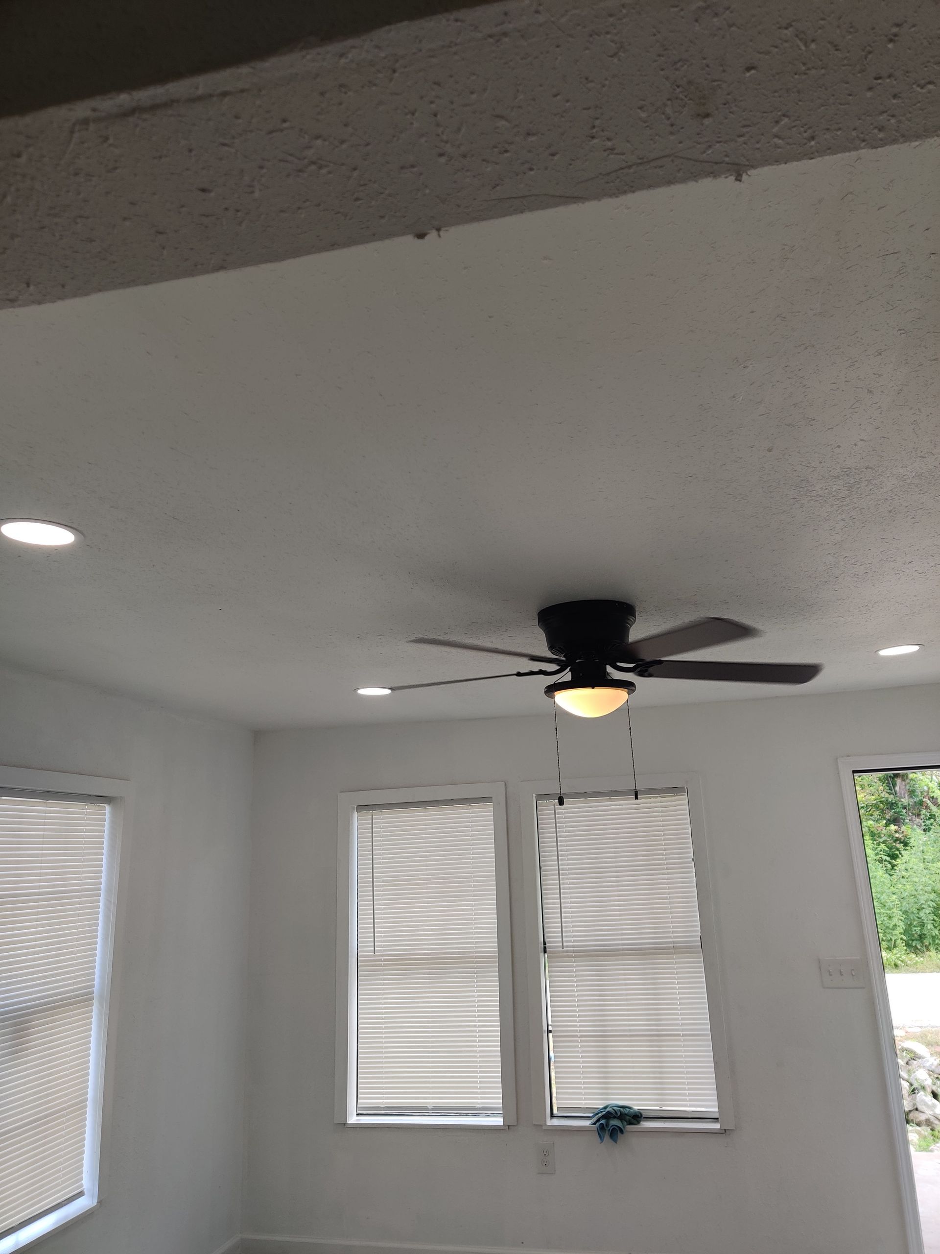 Interior view of a white room with a ceiling fan, recessed lights, and two windows with blinds.