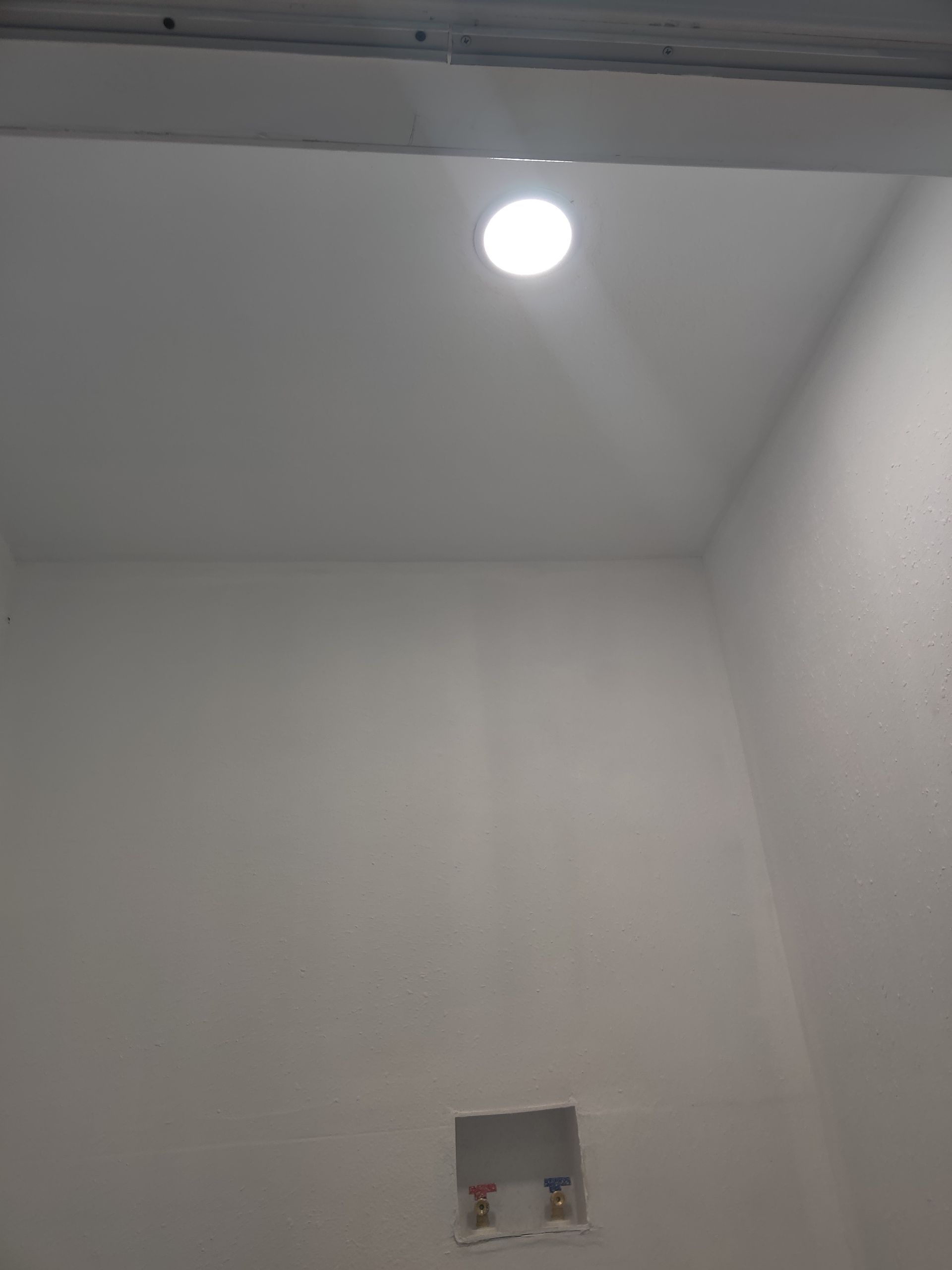 White laundry room interior with recessed light, exposed utility connections on wall.