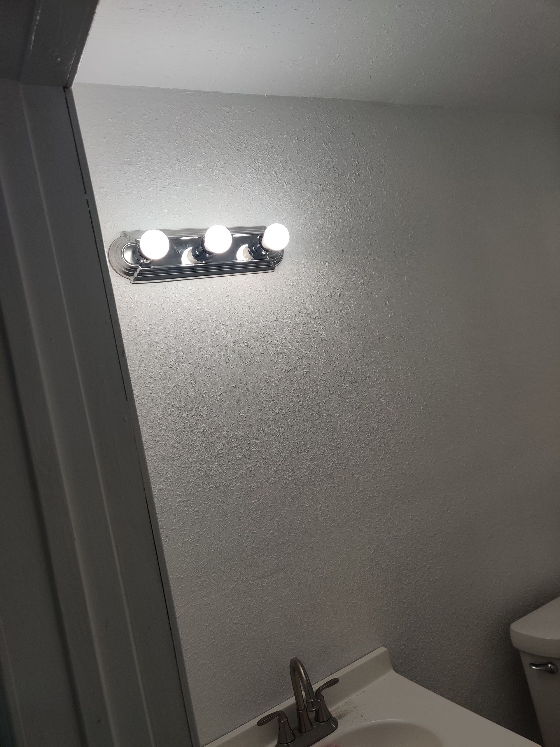 Bathroom with a vanity and a light fixture on a textured wall.