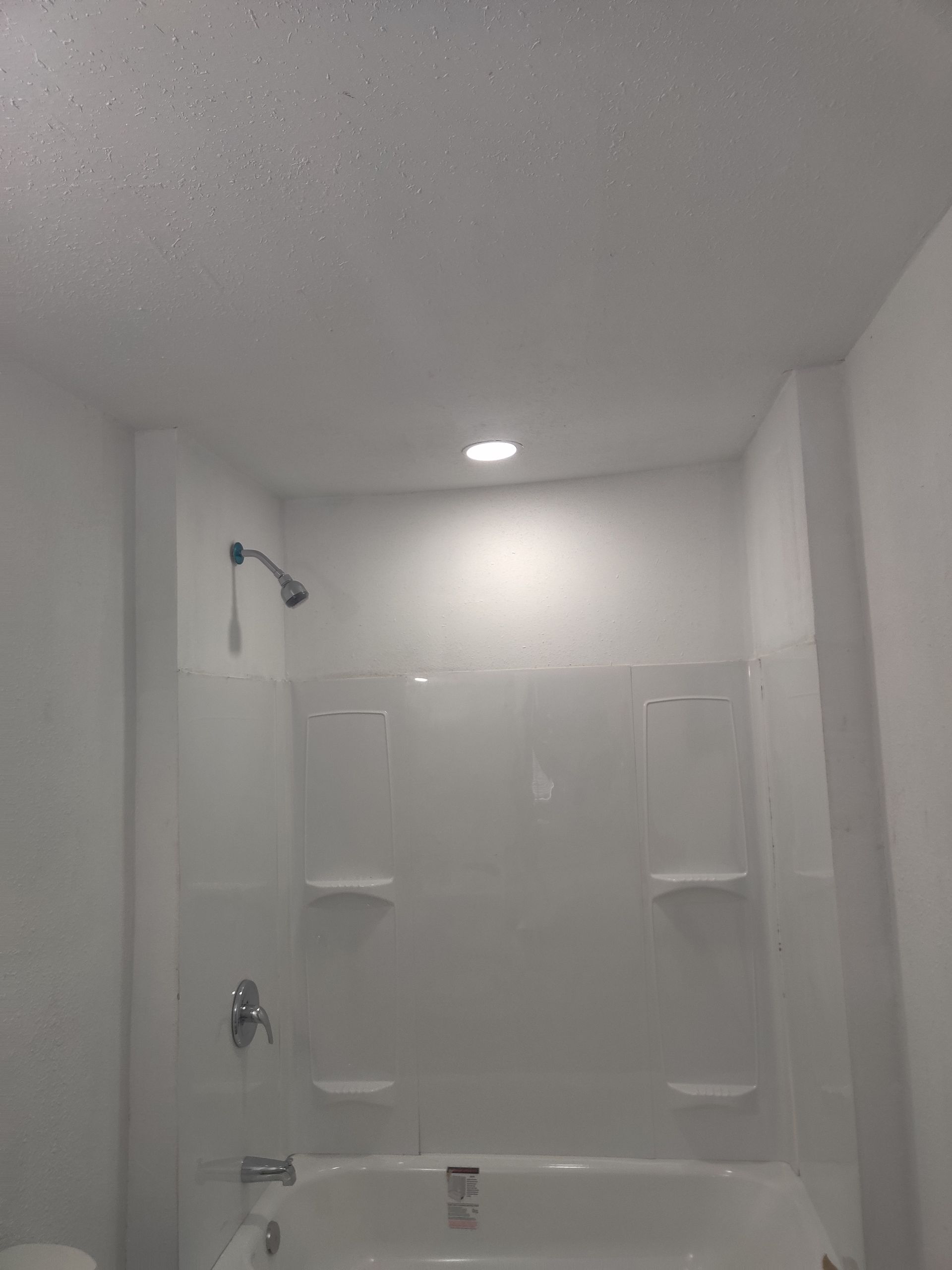 White bathroom with shower and tub, overhead light, white shower surround.