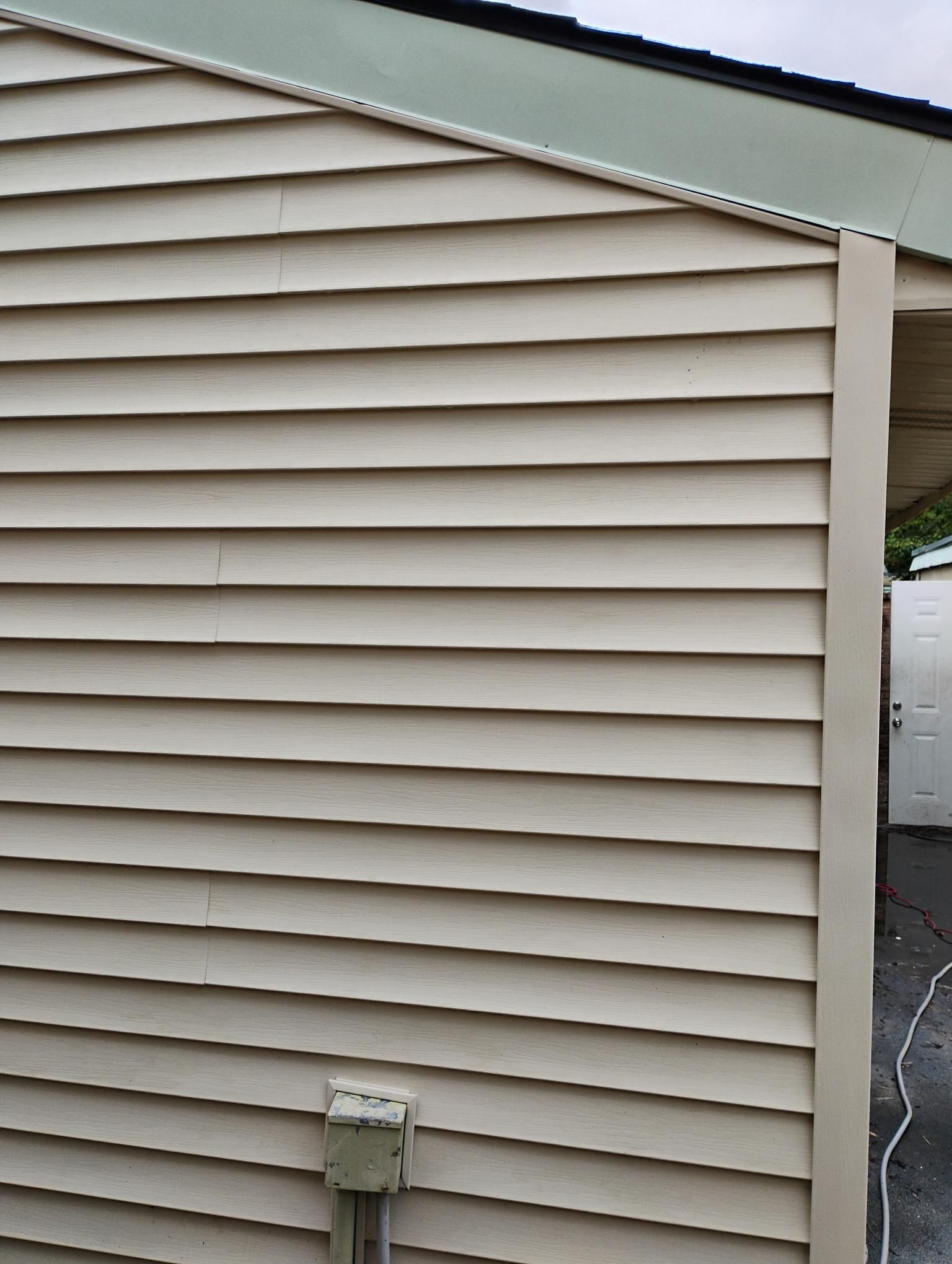 Beige vinyl siding on a building with a corner post. A metal roof is visible.
