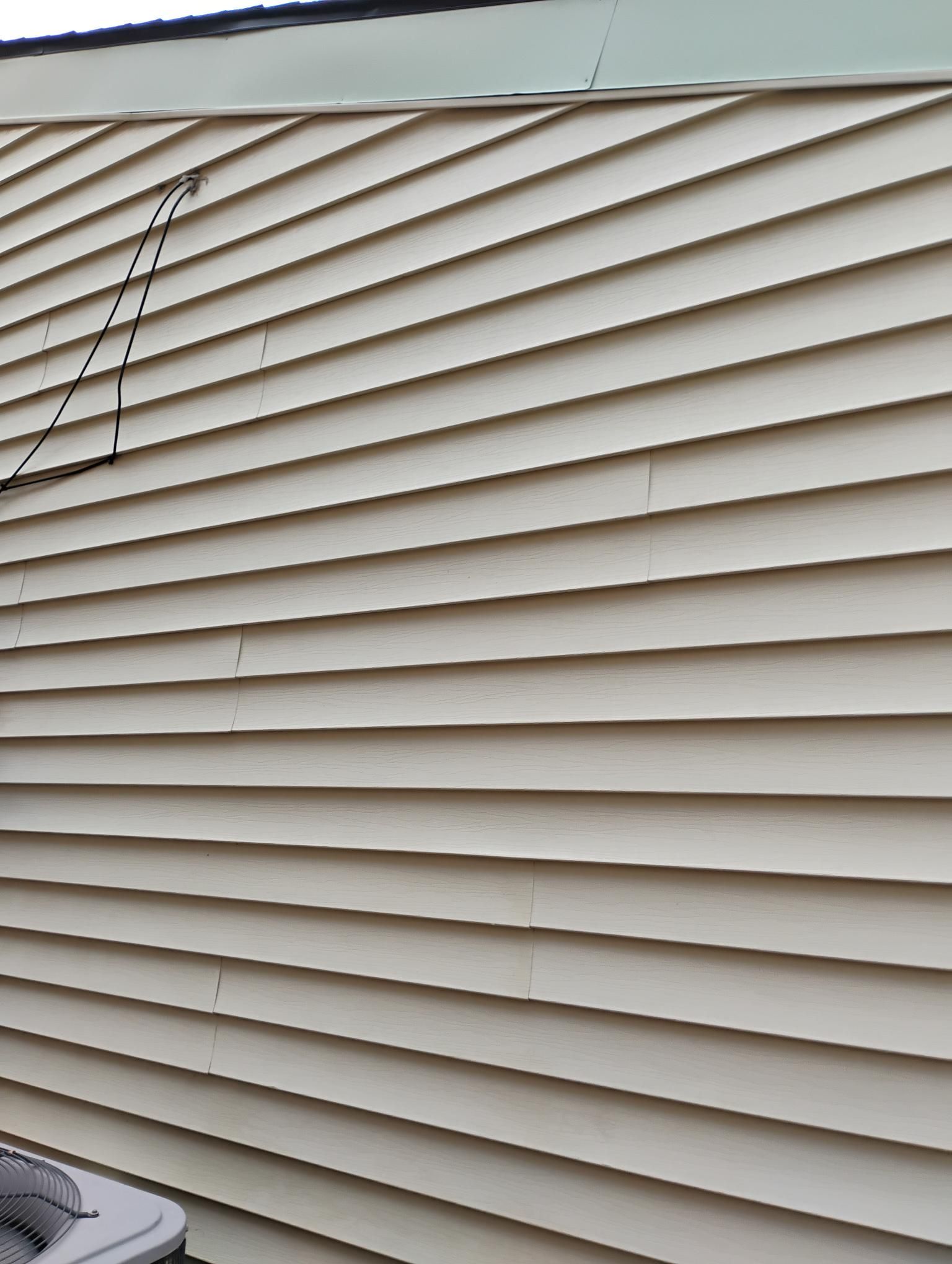 Beige horizontal siding on a building with a black wire and small cracks.