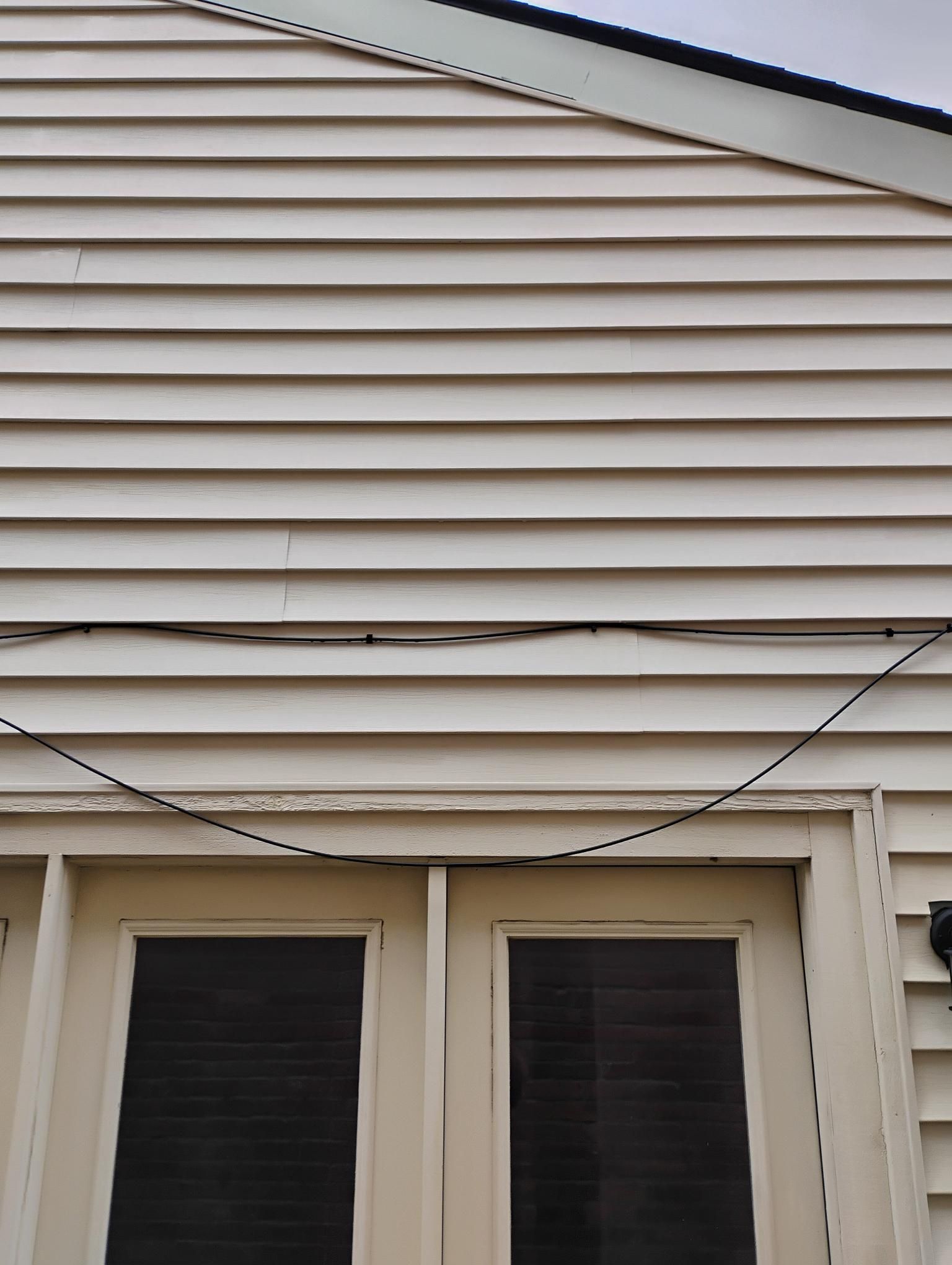 Cream-colored siding above a pair of doors with dark windowpanes; a black wire runs horizontally.