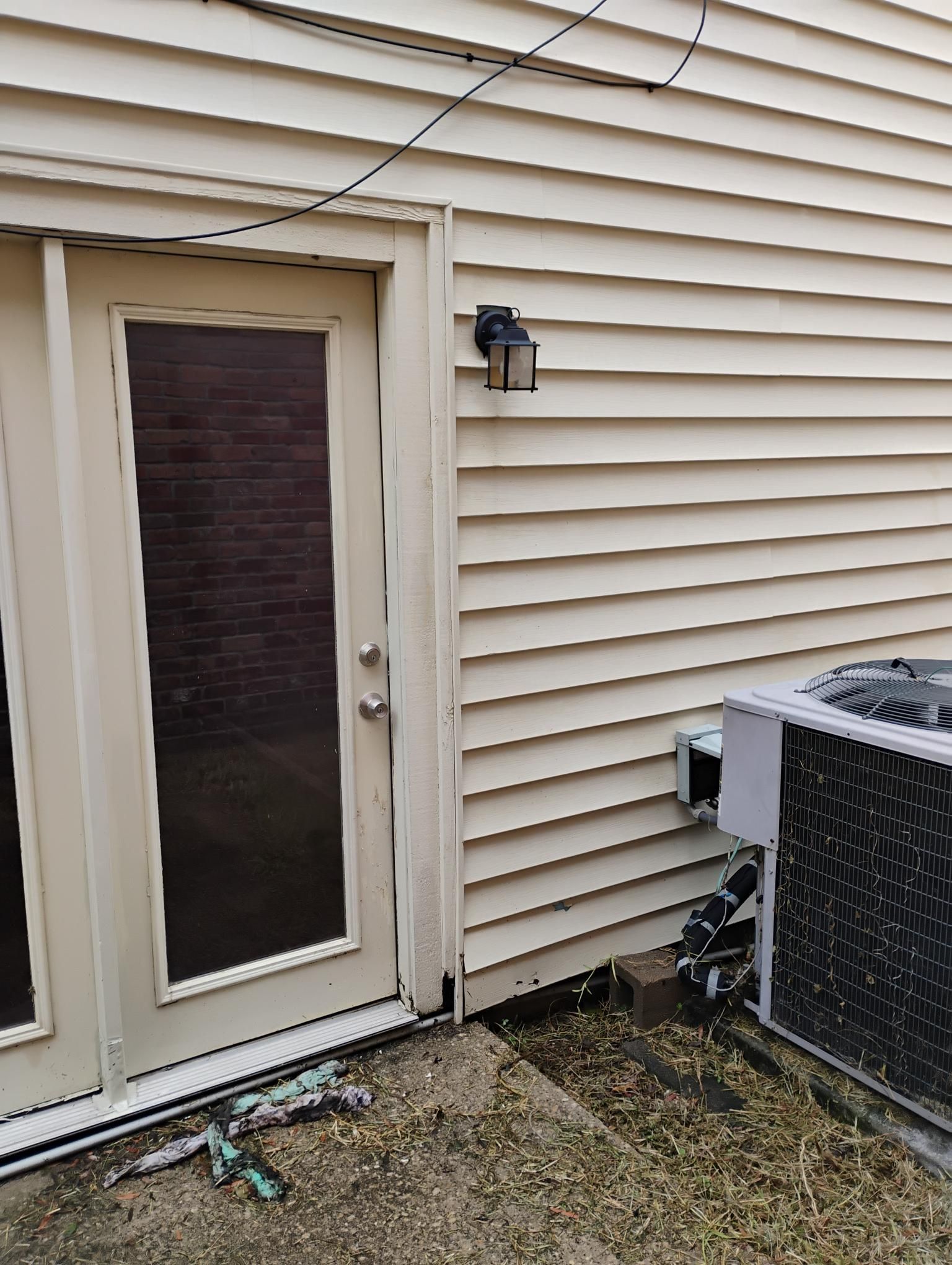 Exterior of a building with a door, air conditioner, and siding. Beige walls, gray patio, and black electrical wire.