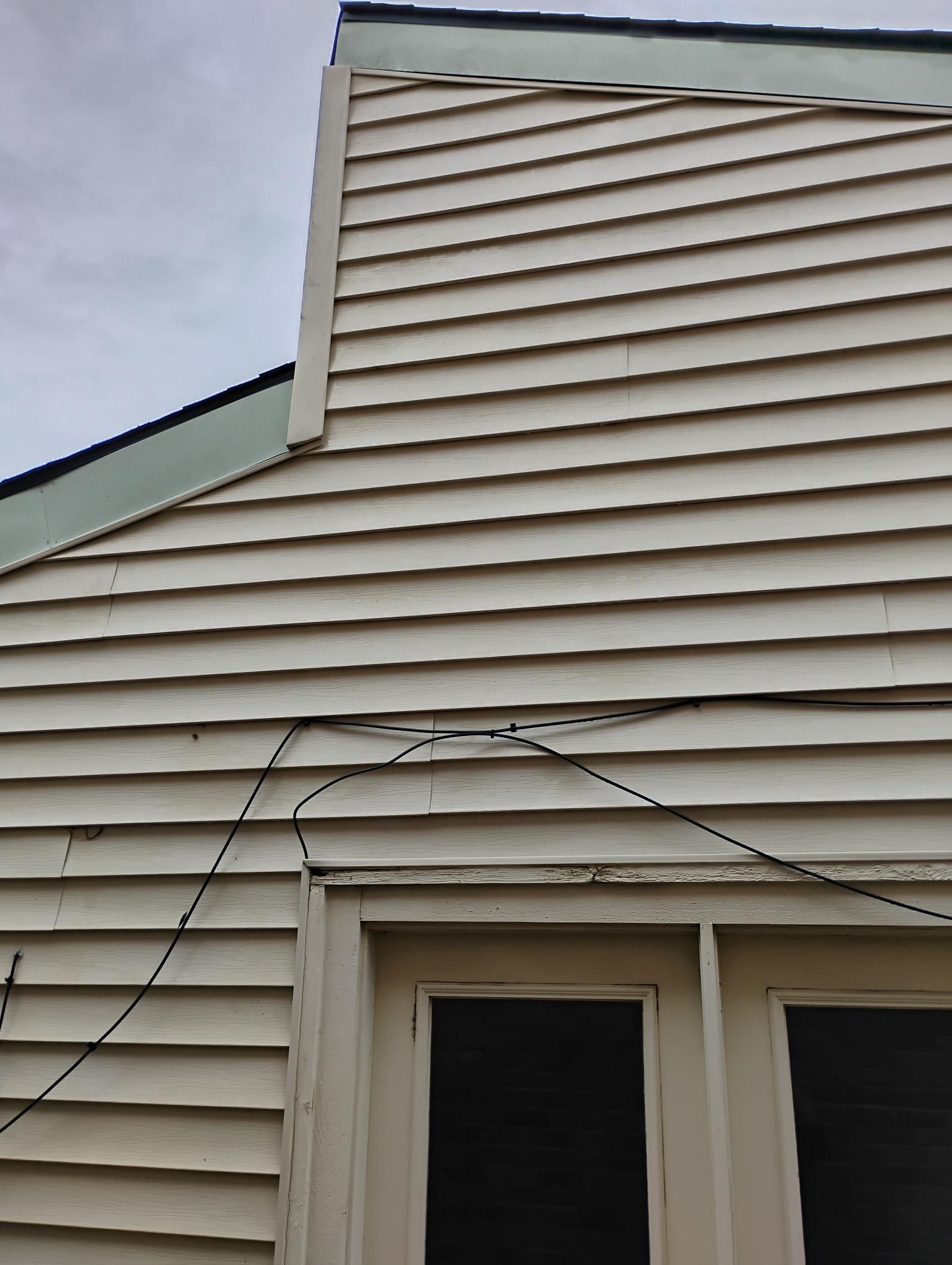 White clapboard siding with a bowed section above a door and window. A black wire runs across the wall.