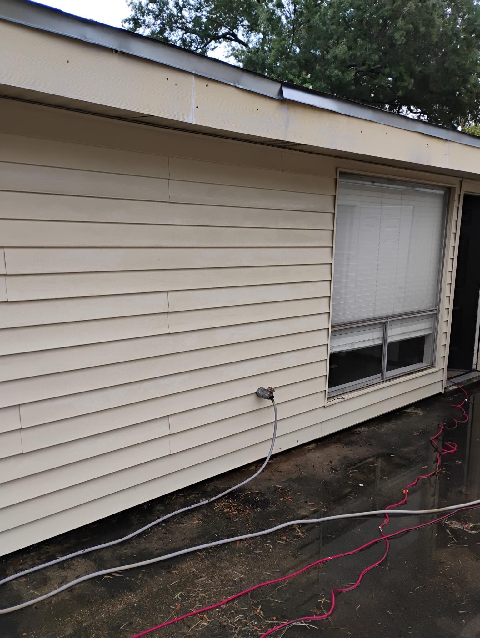 Beige siding on a building with a window and electrical wires on wet ground.