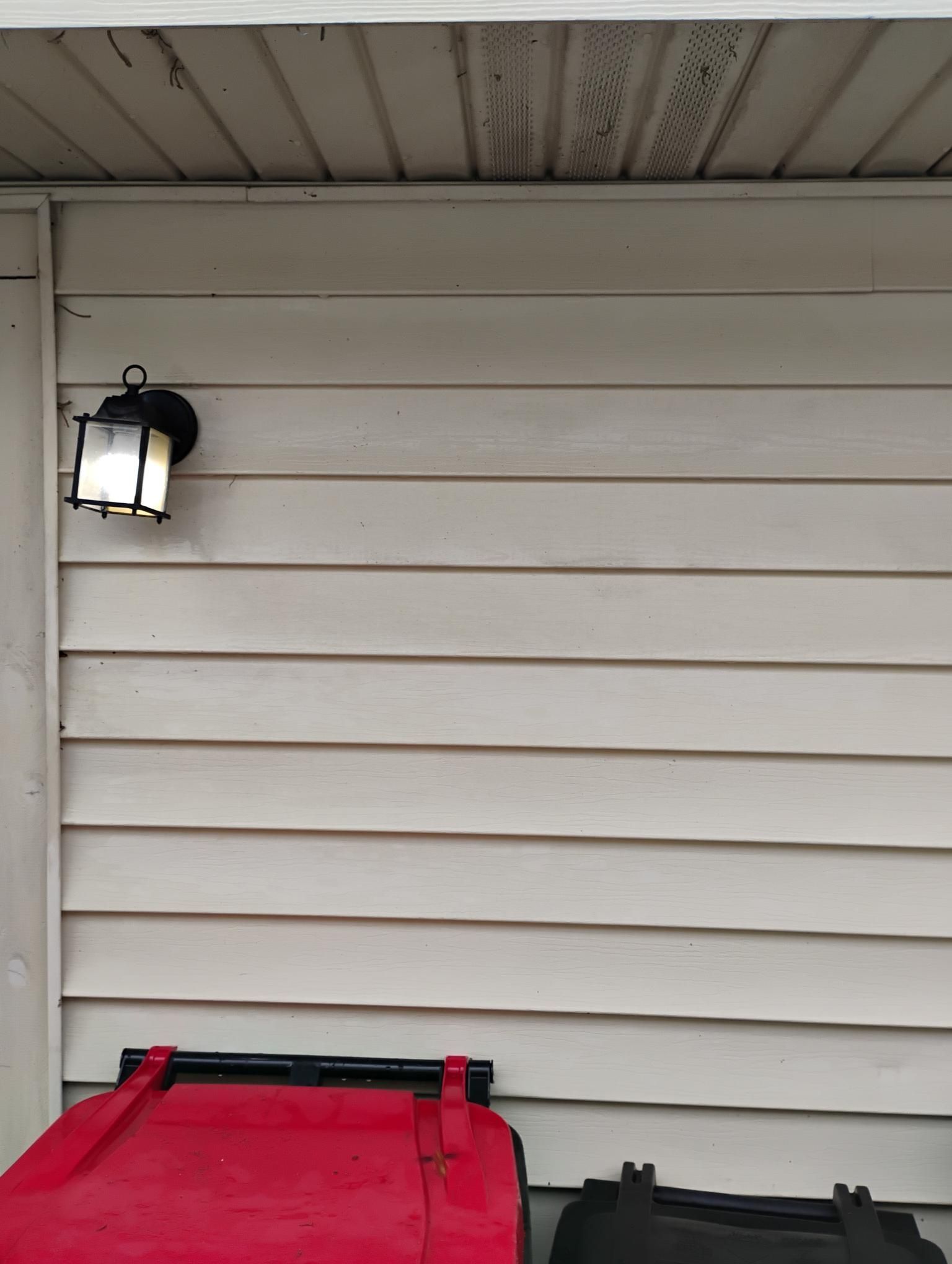 Outdoor wall with a lit black lantern and two trash bins below.
