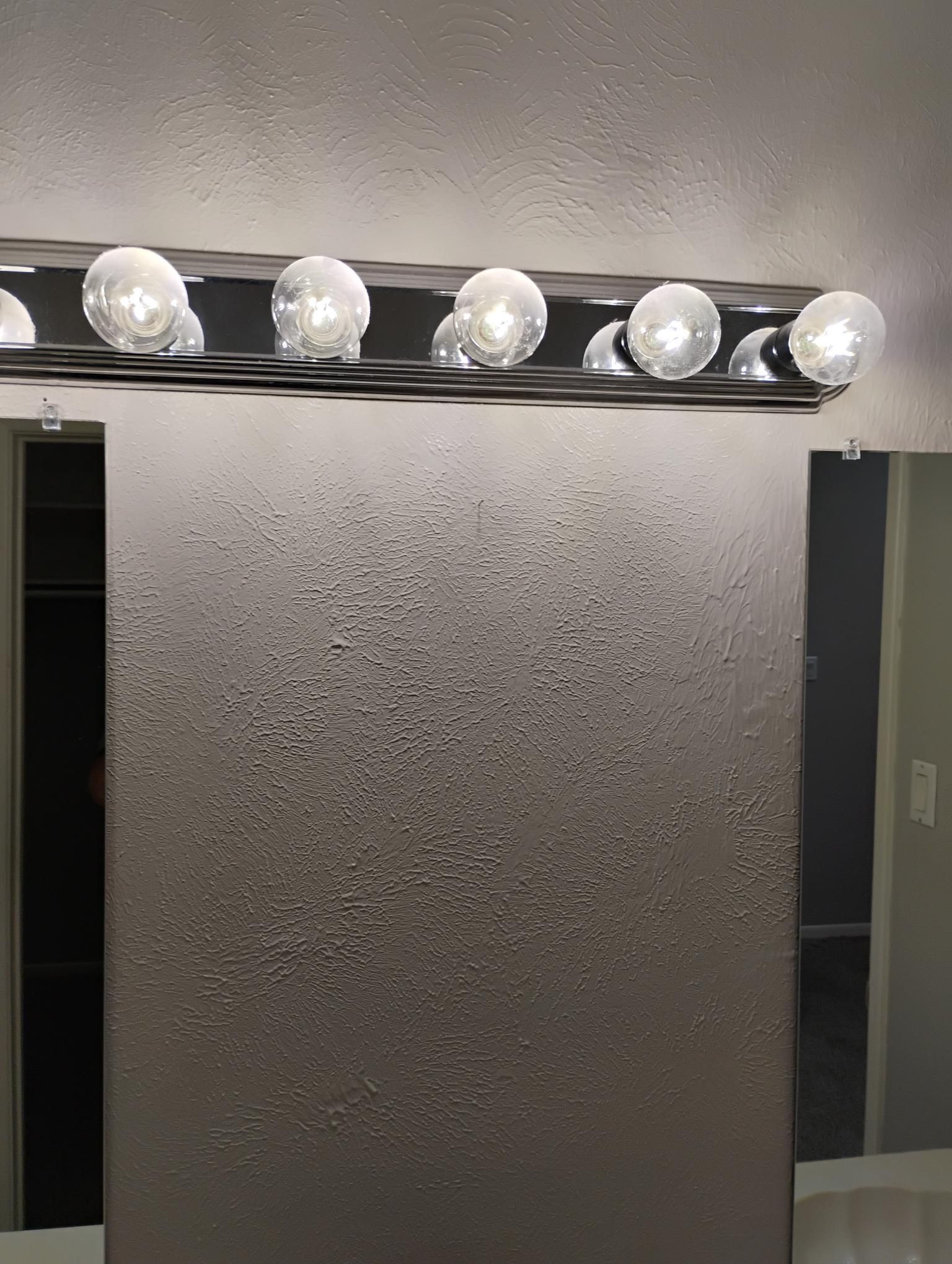 Vanity mirror with textured gray surface, lit by a row of seven bright bulbs.