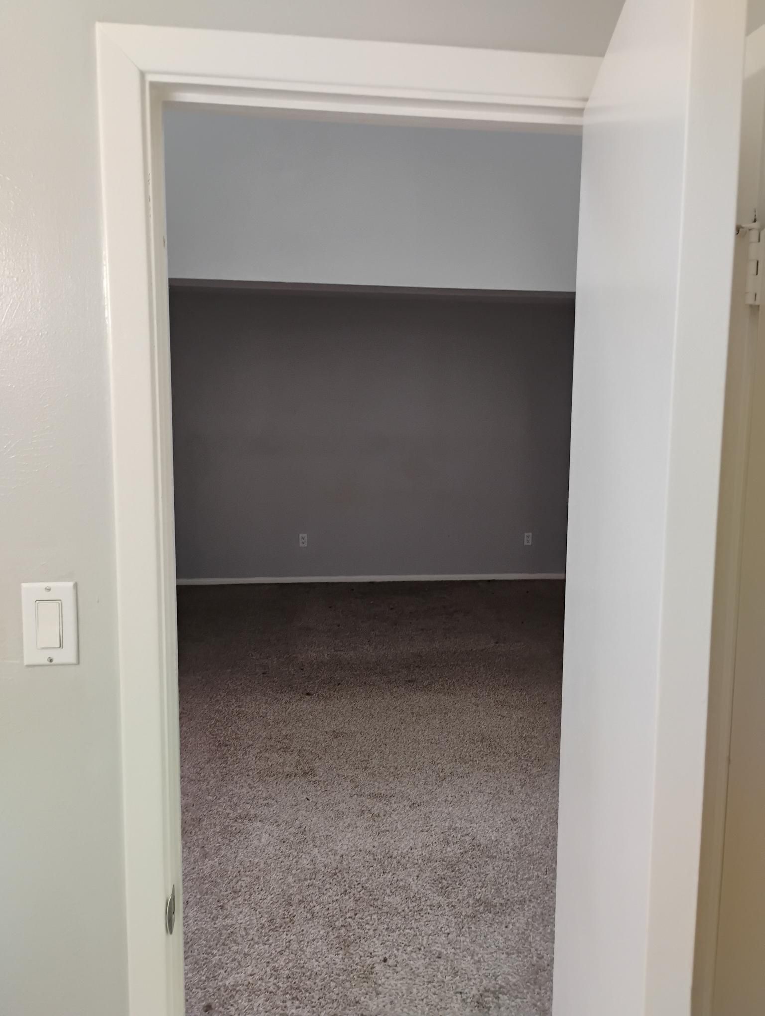 Doorway into a room with gray walls and carpet. Light switch on the left.