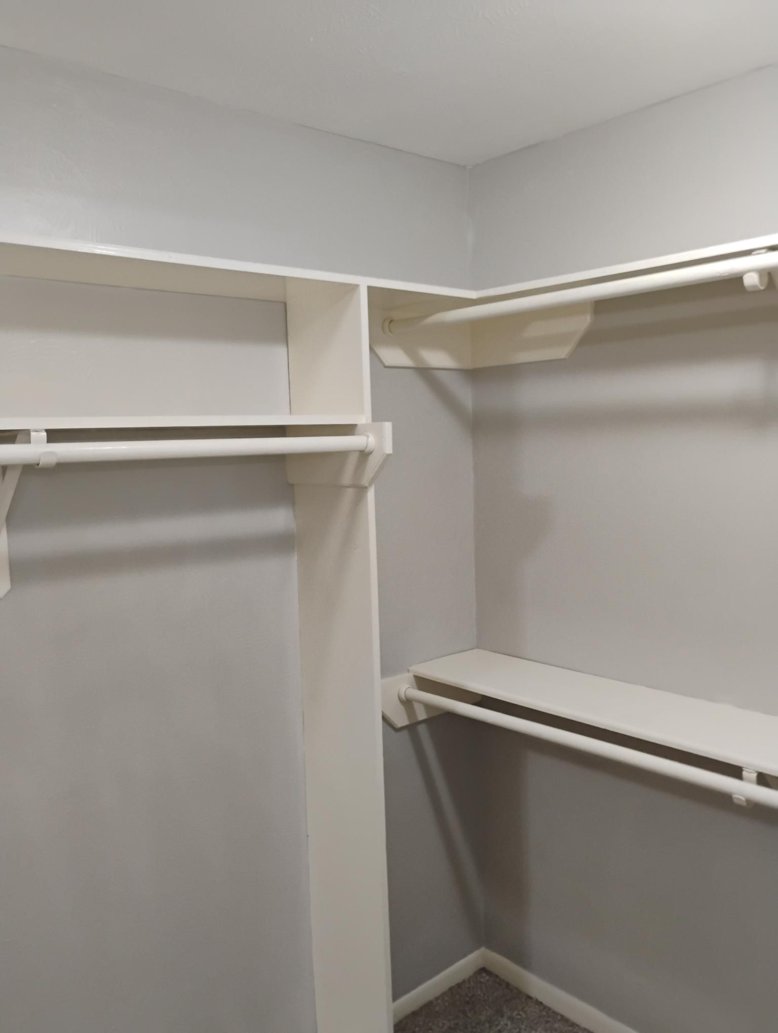 Empty walk-in closet with white shelves and rods against gray walls.
