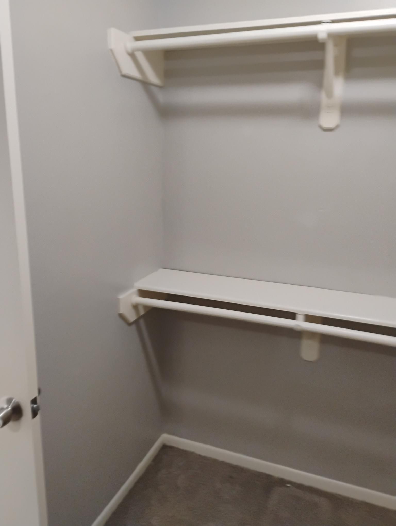 Empty closet with gray walls, white shelves and a closet rod.