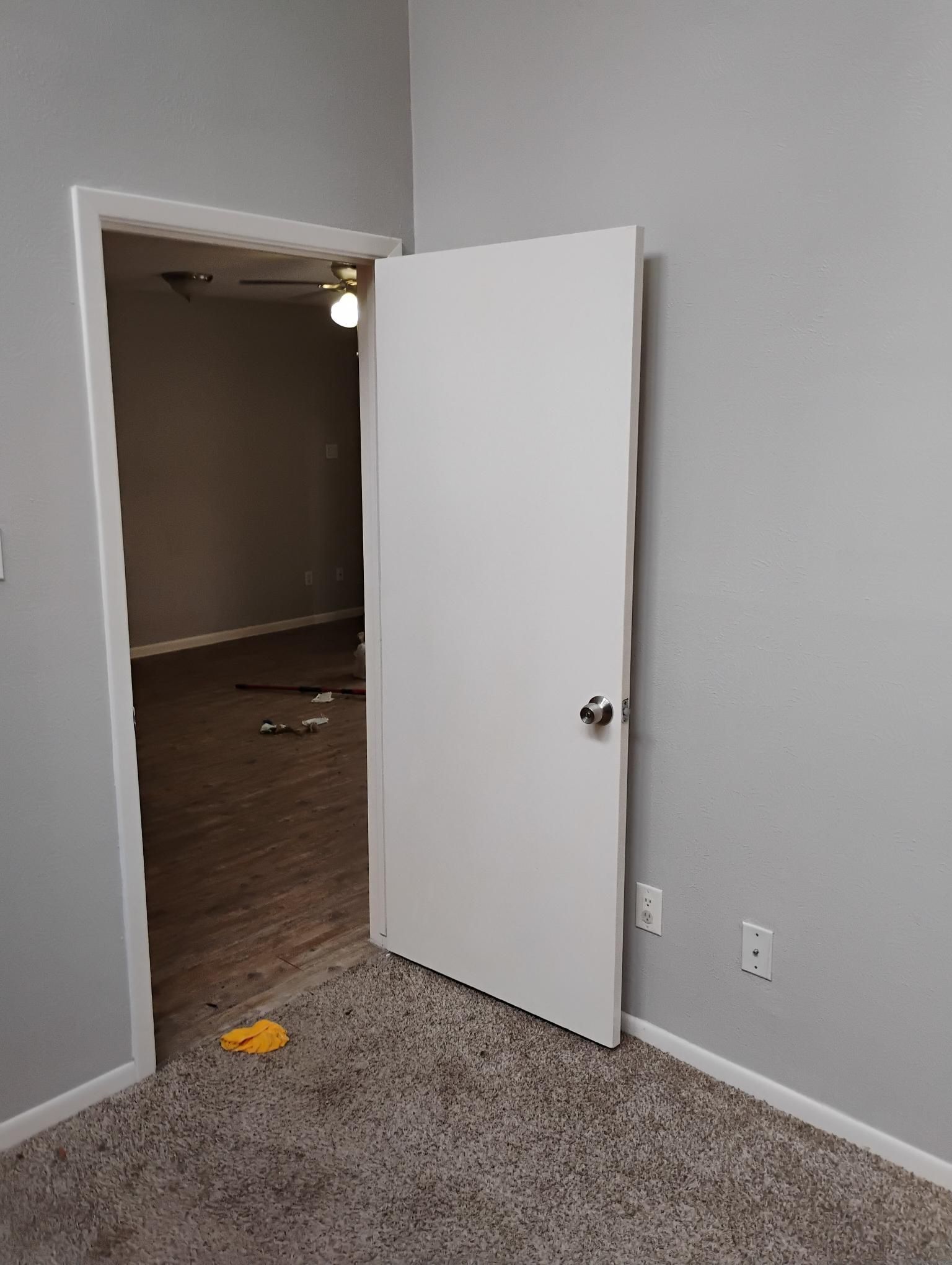 White door ajar, leading to a room with hardwood floors. The room has gray walls and a ceiling fan.