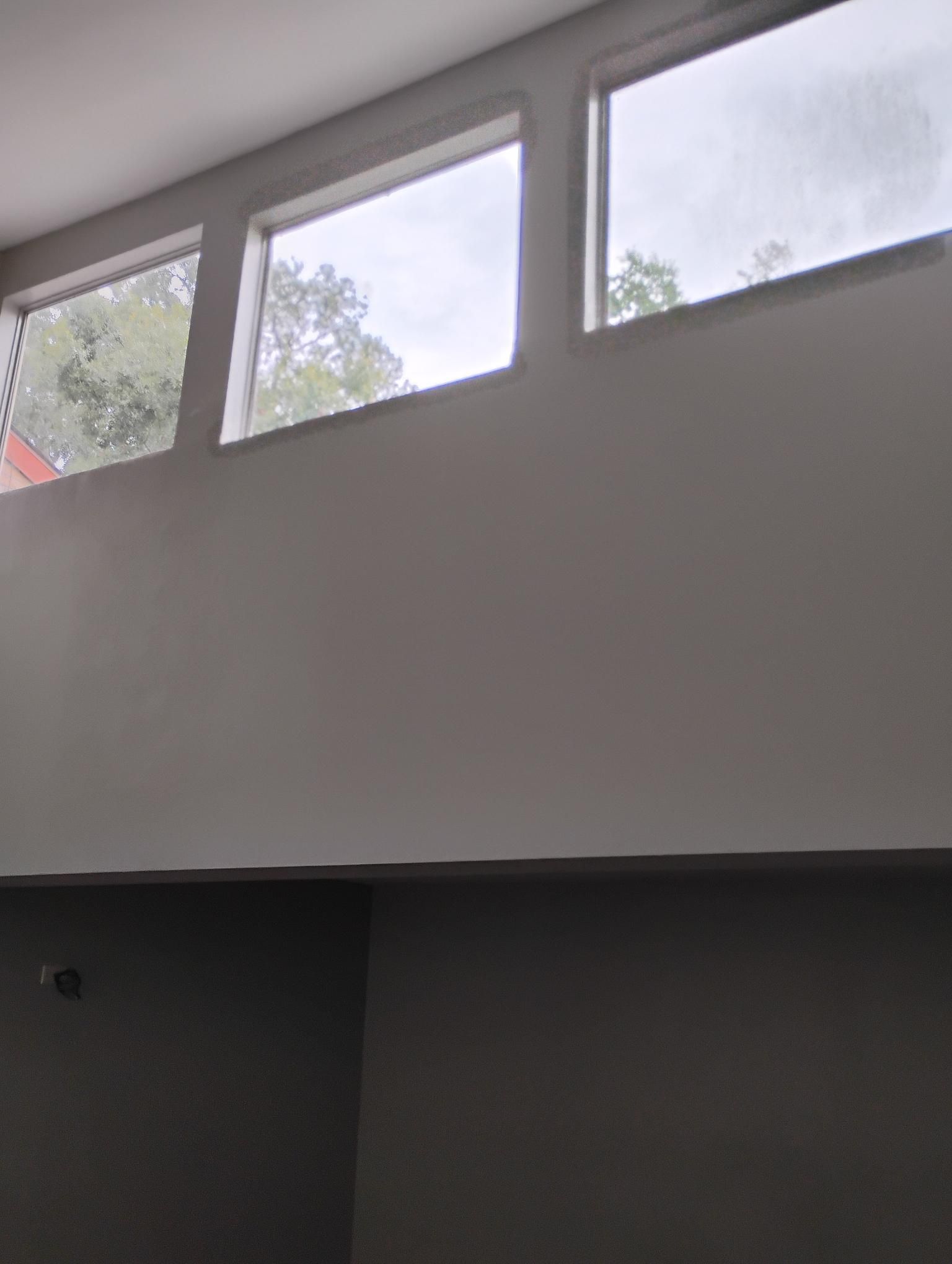 Three rectangular windows above a tall gray wall, interior view, cloudy outdoor view.