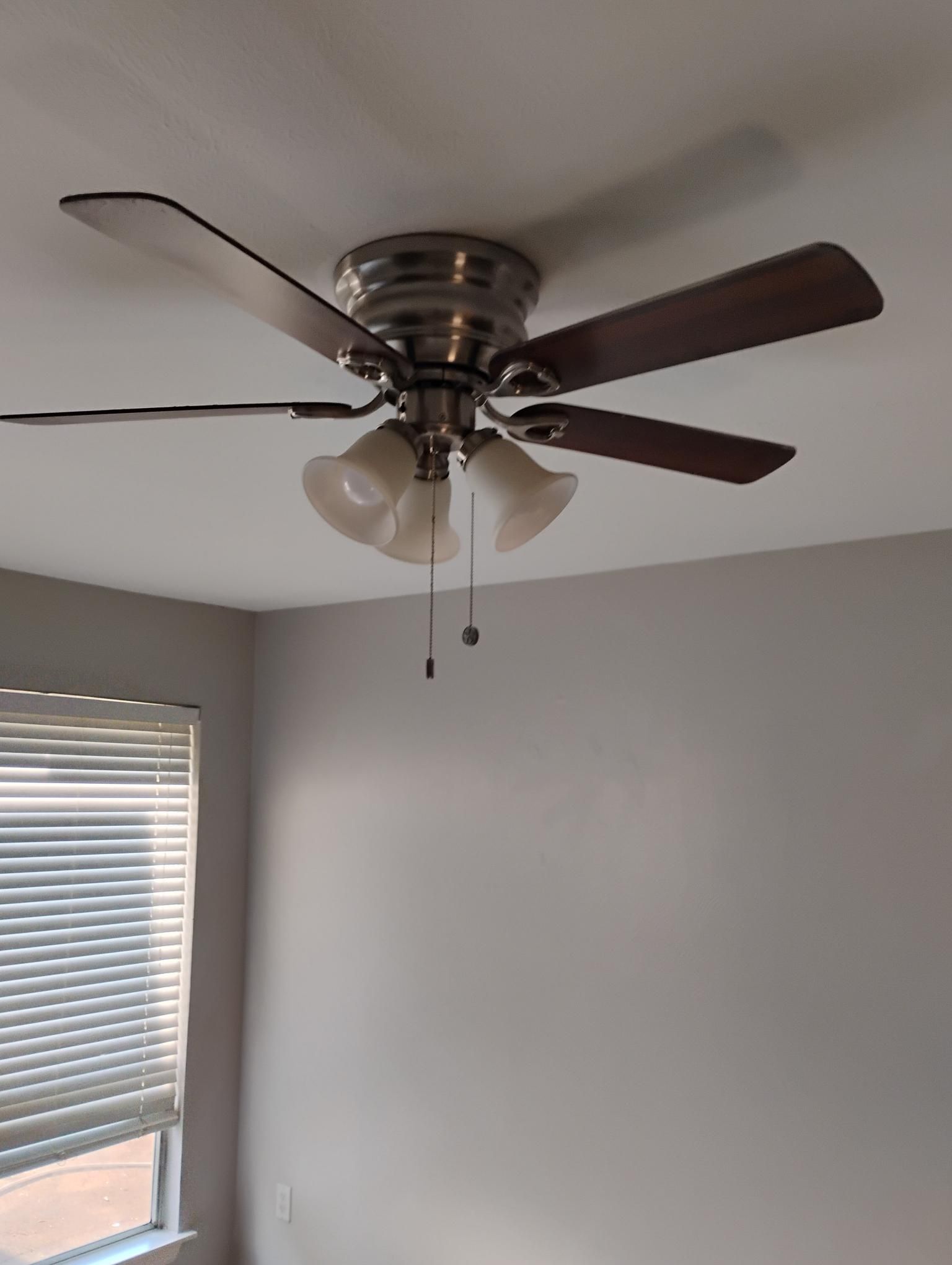 Ceiling fan with wooden blades and three lights in a room with a window and blinds.