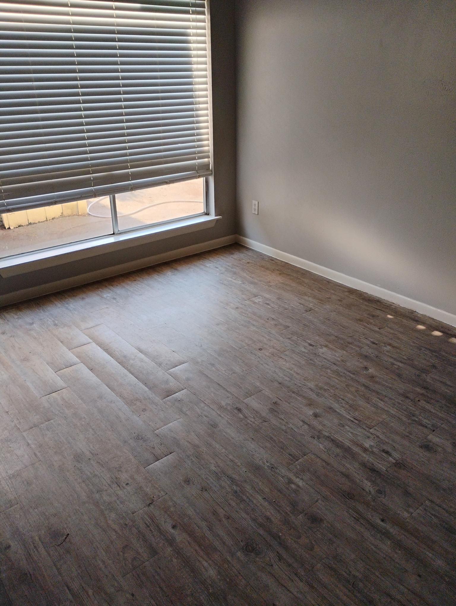 Empty room with wood-look floor, window with blinds, and light gray walls.
