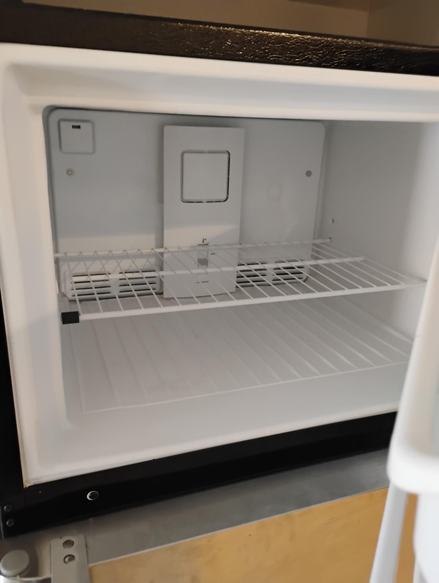 Empty, open mini-refrigerator. White interior with one shelf, a rectangular compartment, and a door on top.