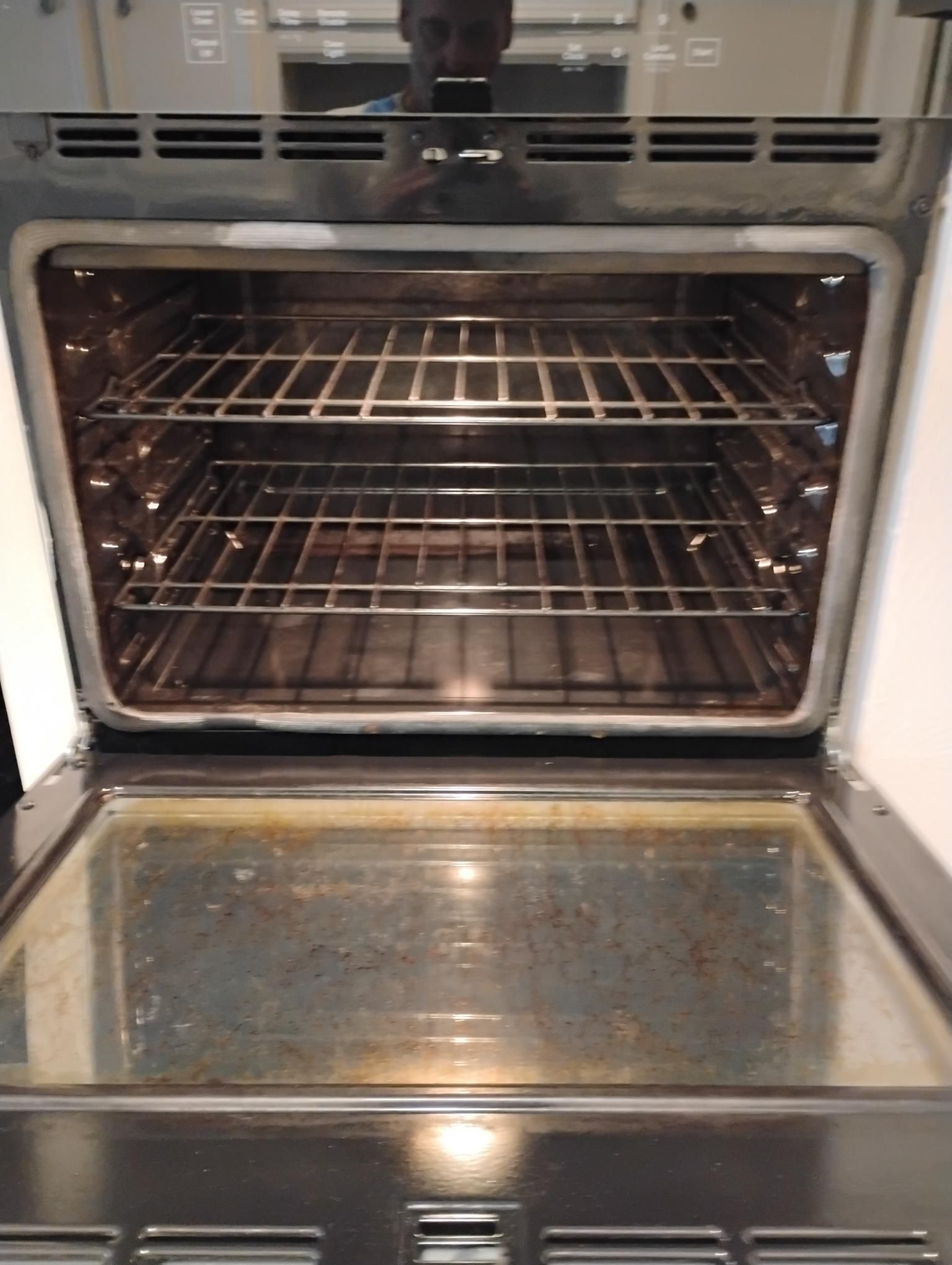 Open oven with two racks inside, a dirty bottom.