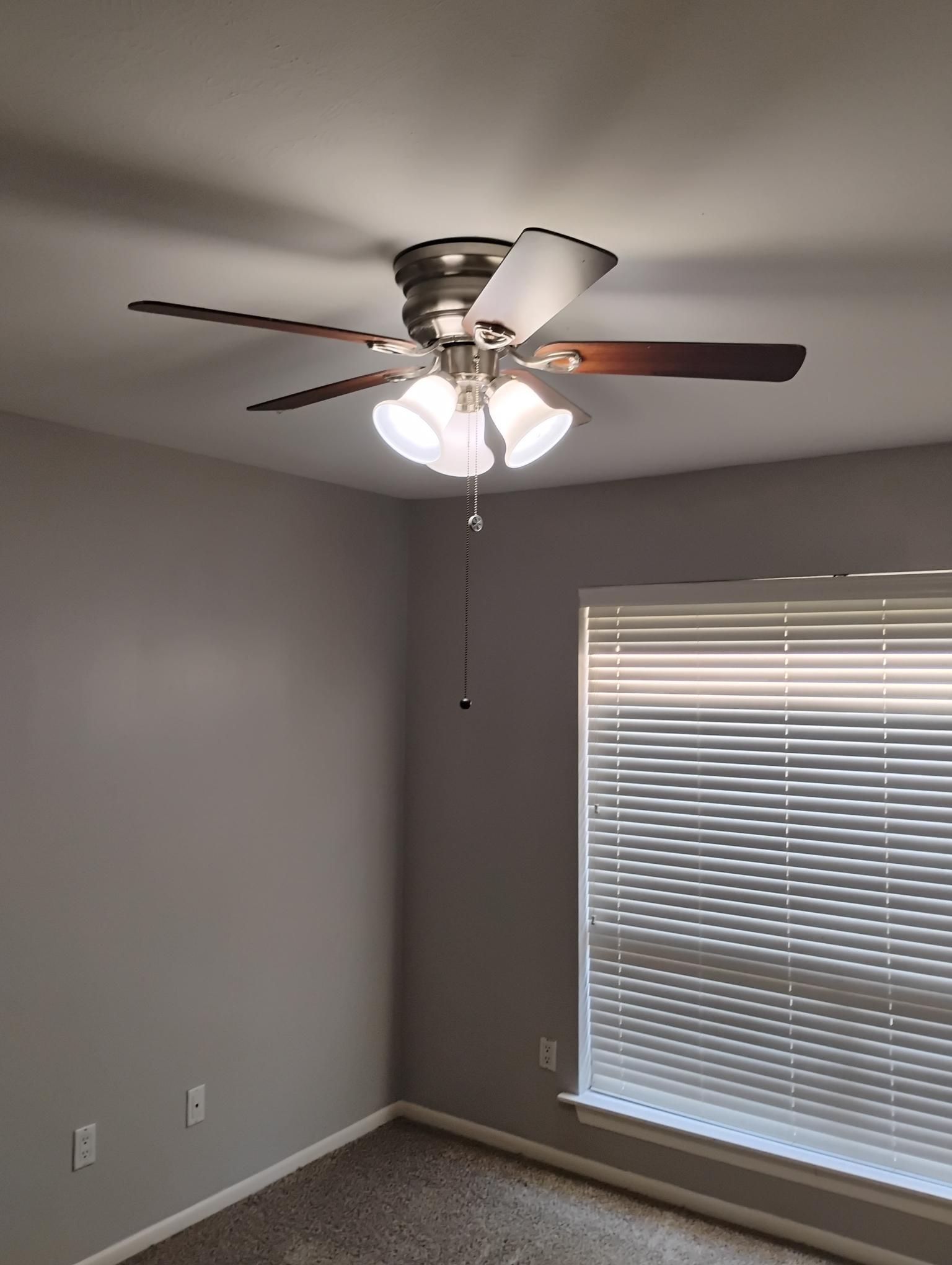 Ceiling fan with lights in a room with a window and gray walls.