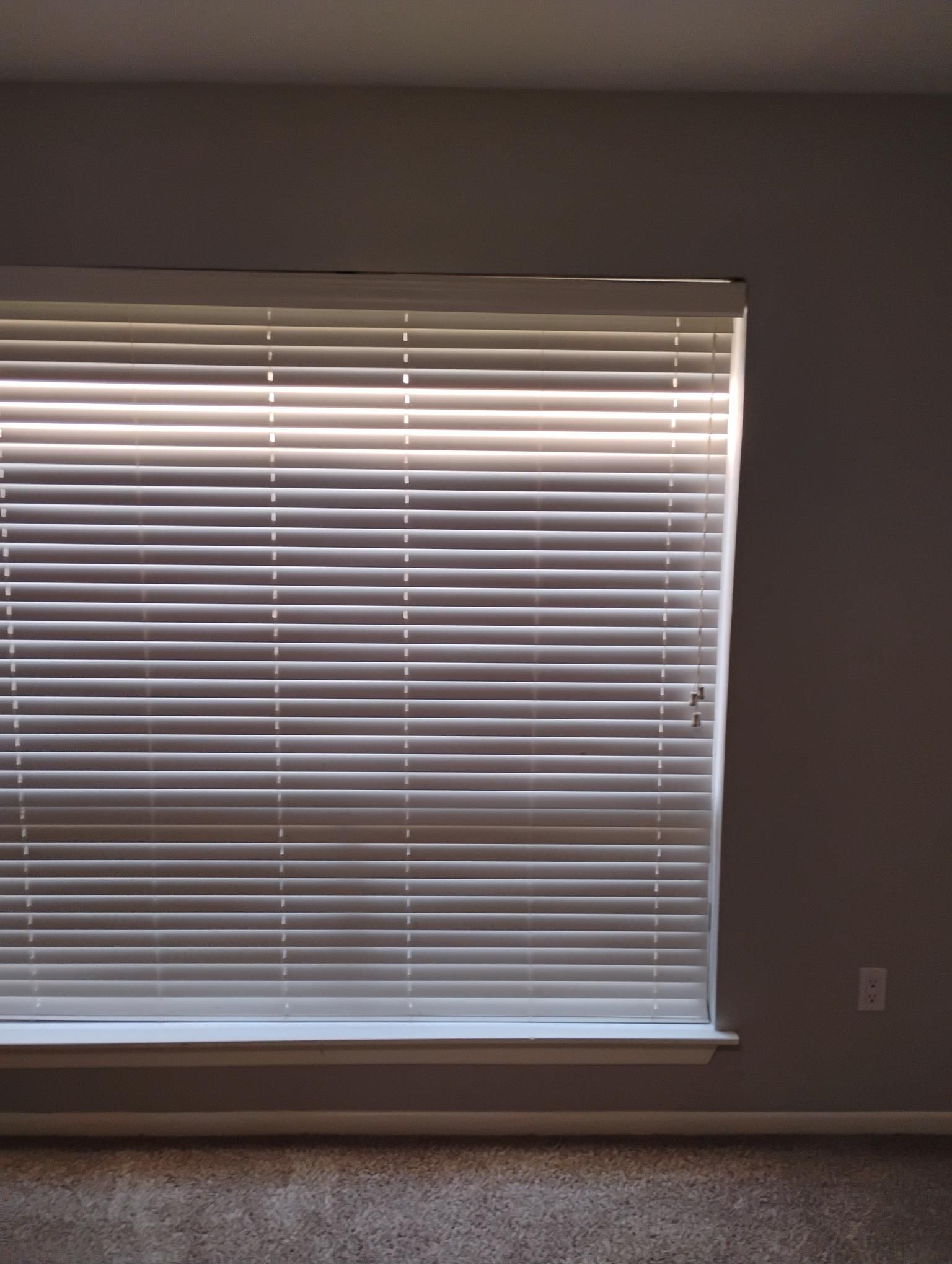 White blinds partially open, casting horizontal light and shadows on a wall.