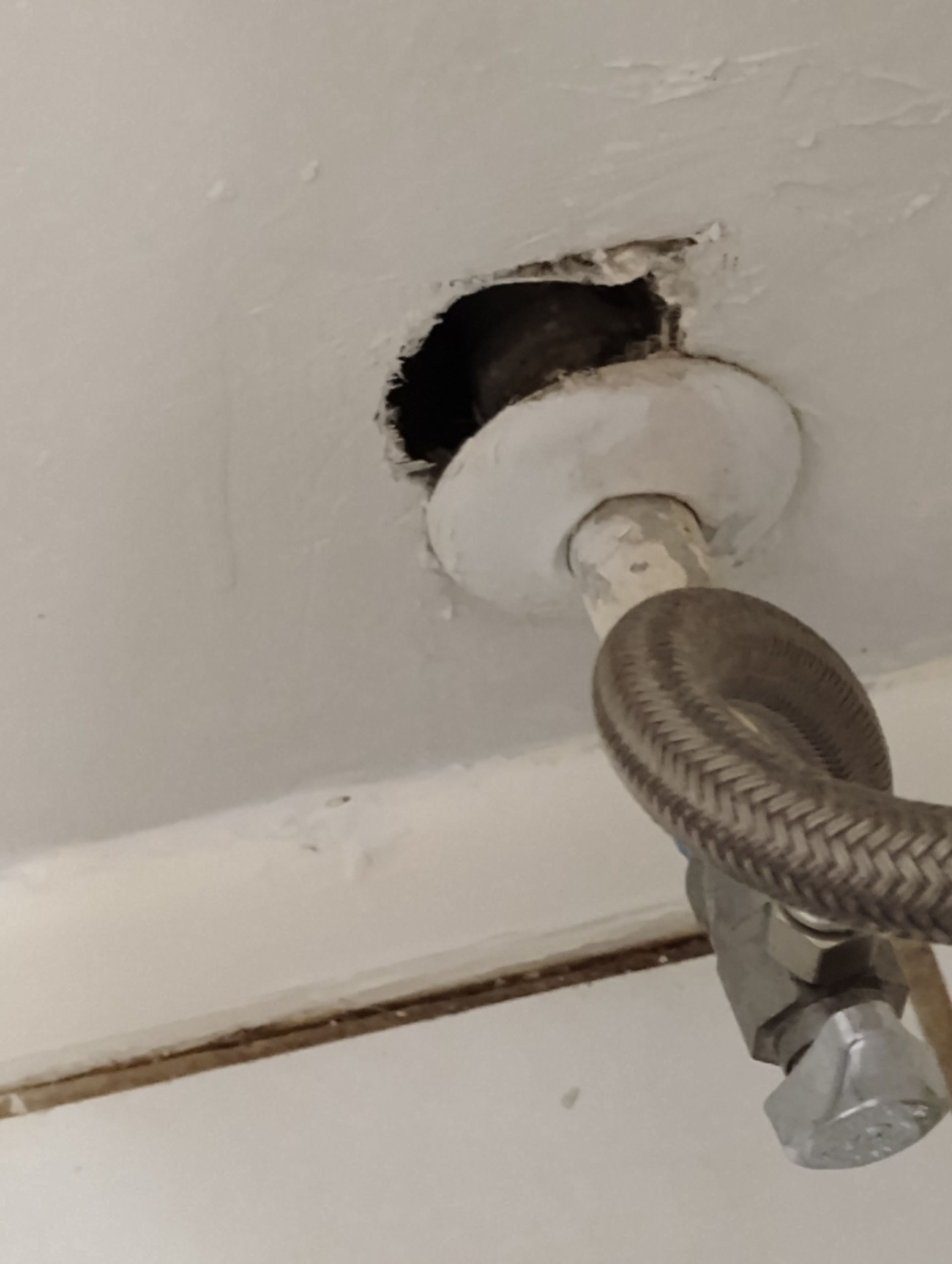 Hole in ceiling with water pipe and valve. White trim, hole is dark. Pipe is silver.