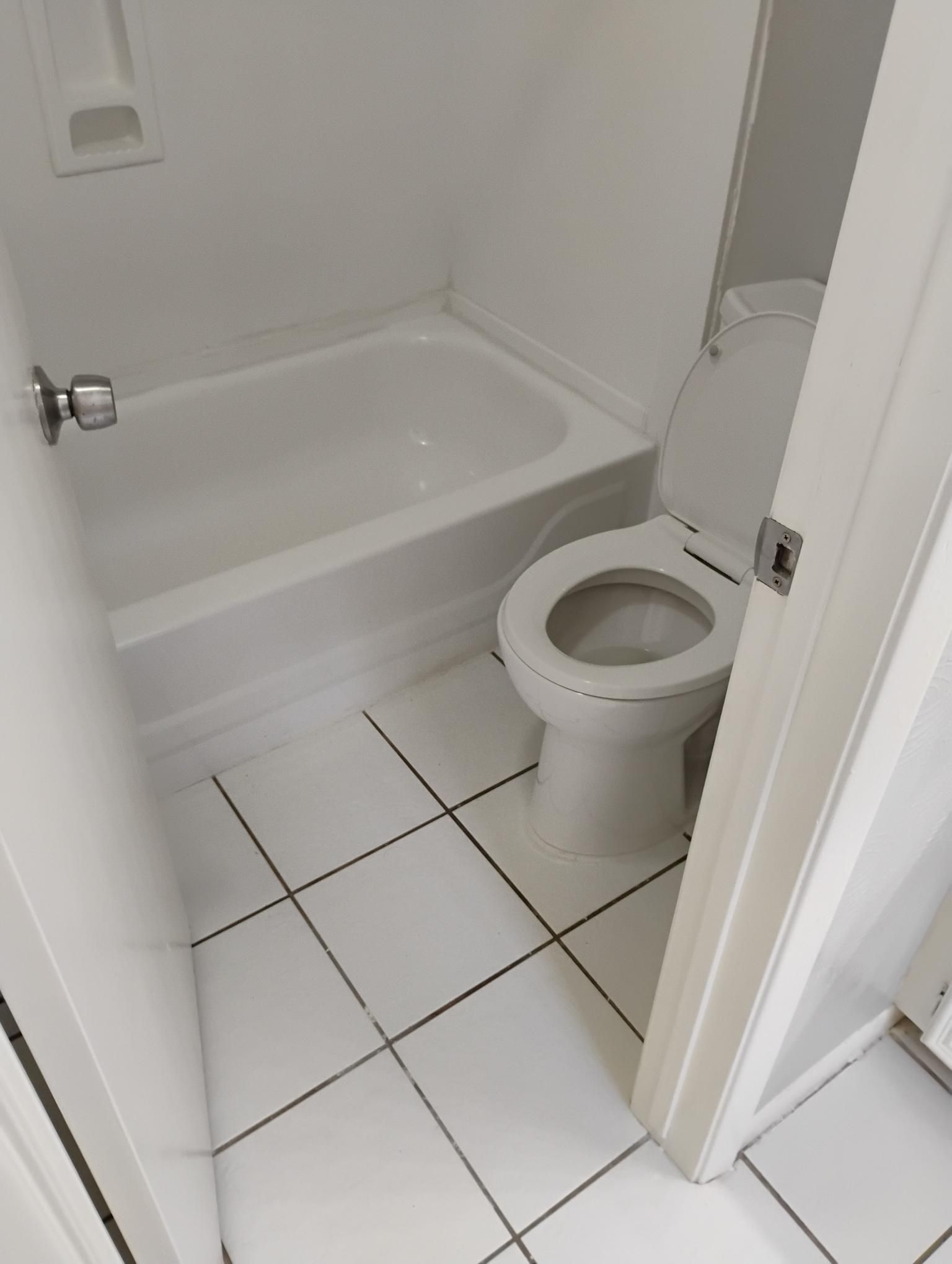 Small white bathroom with a tub, toilet, and tiled floor.