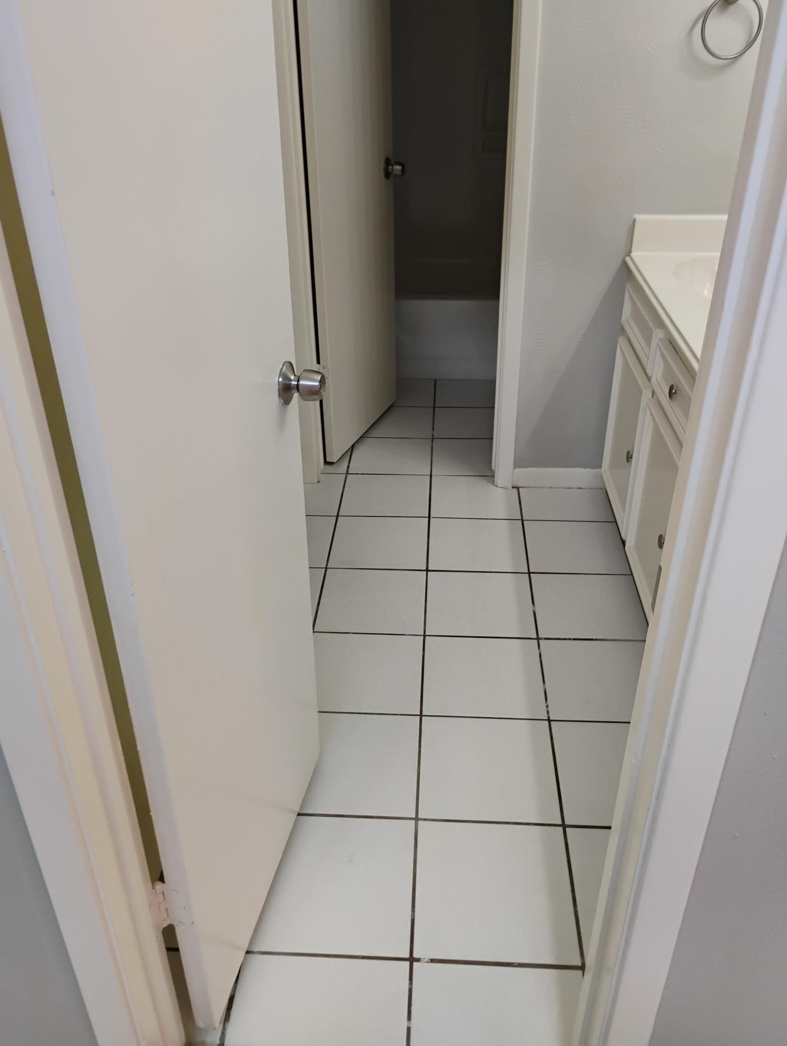 Bathroom interior with white tile floor, partially open door, and vanity.