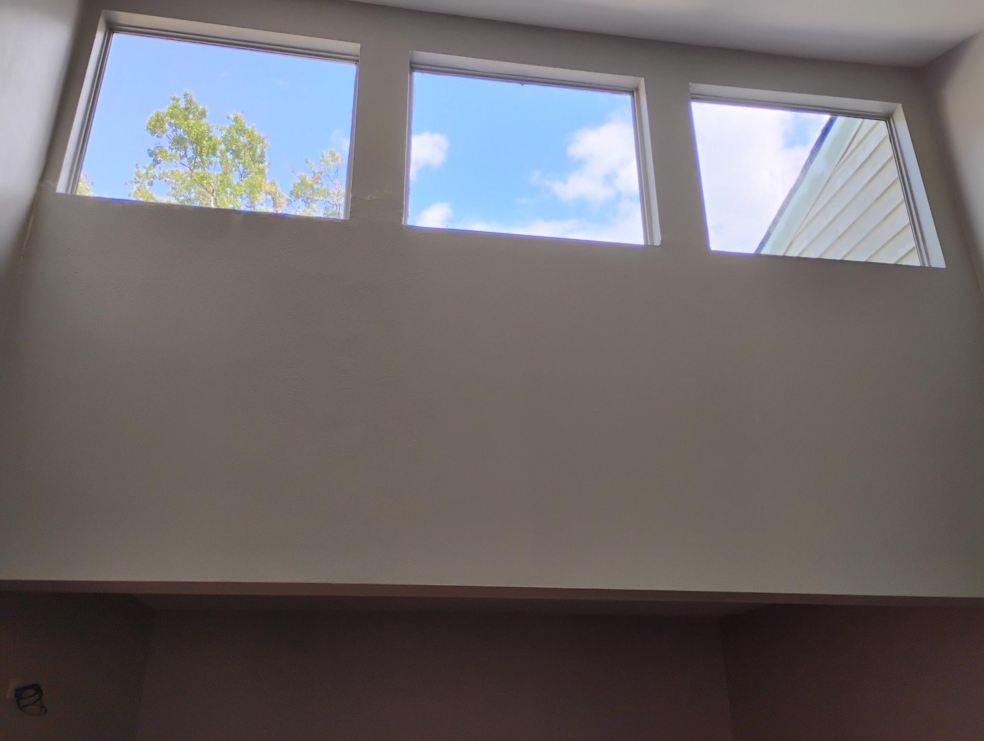 Three square windows high on a white wall, revealing a bright blue sky with clouds.