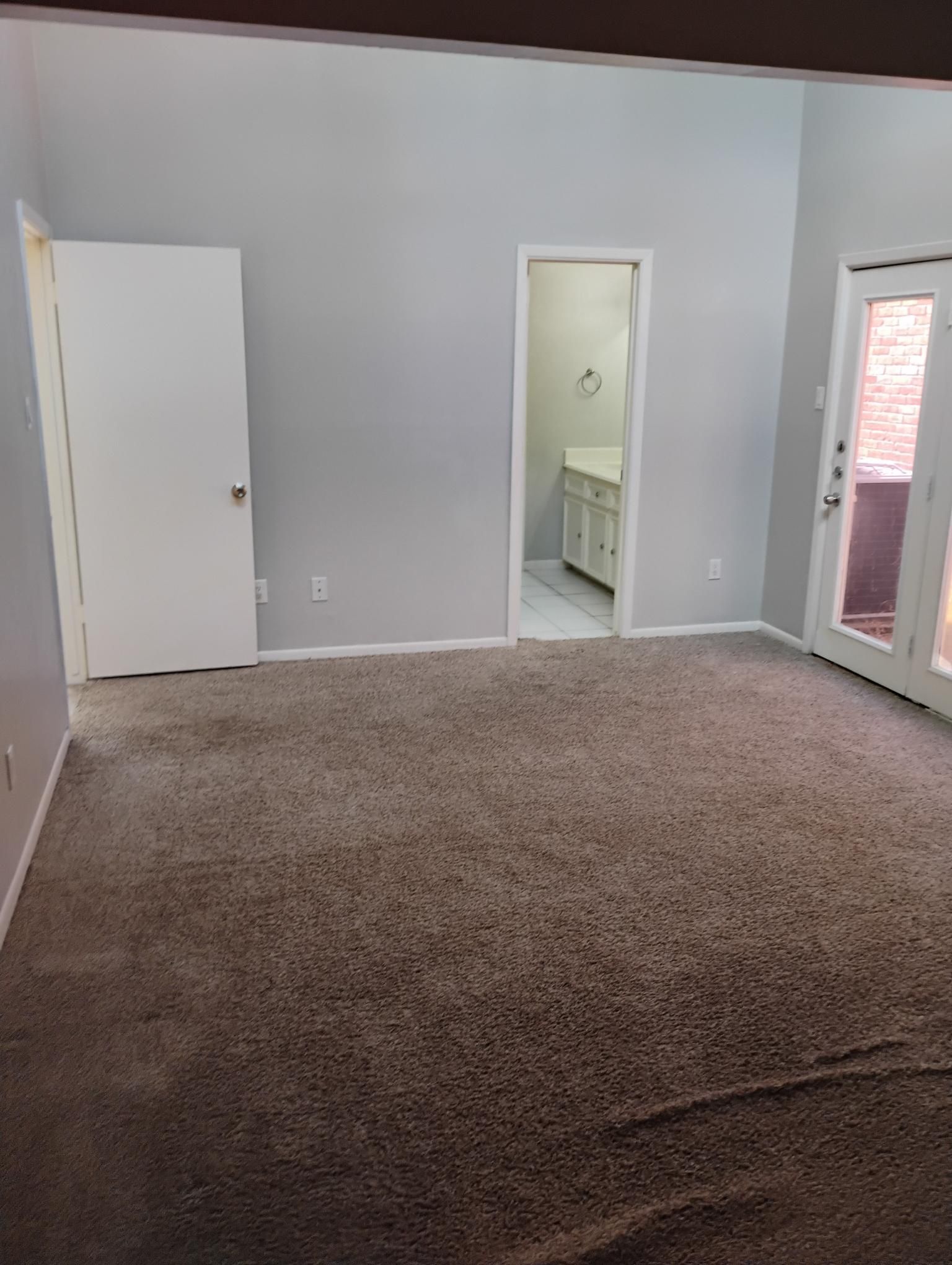 Empty room with gray walls, brown carpet, white doors, and a bathroom visible.