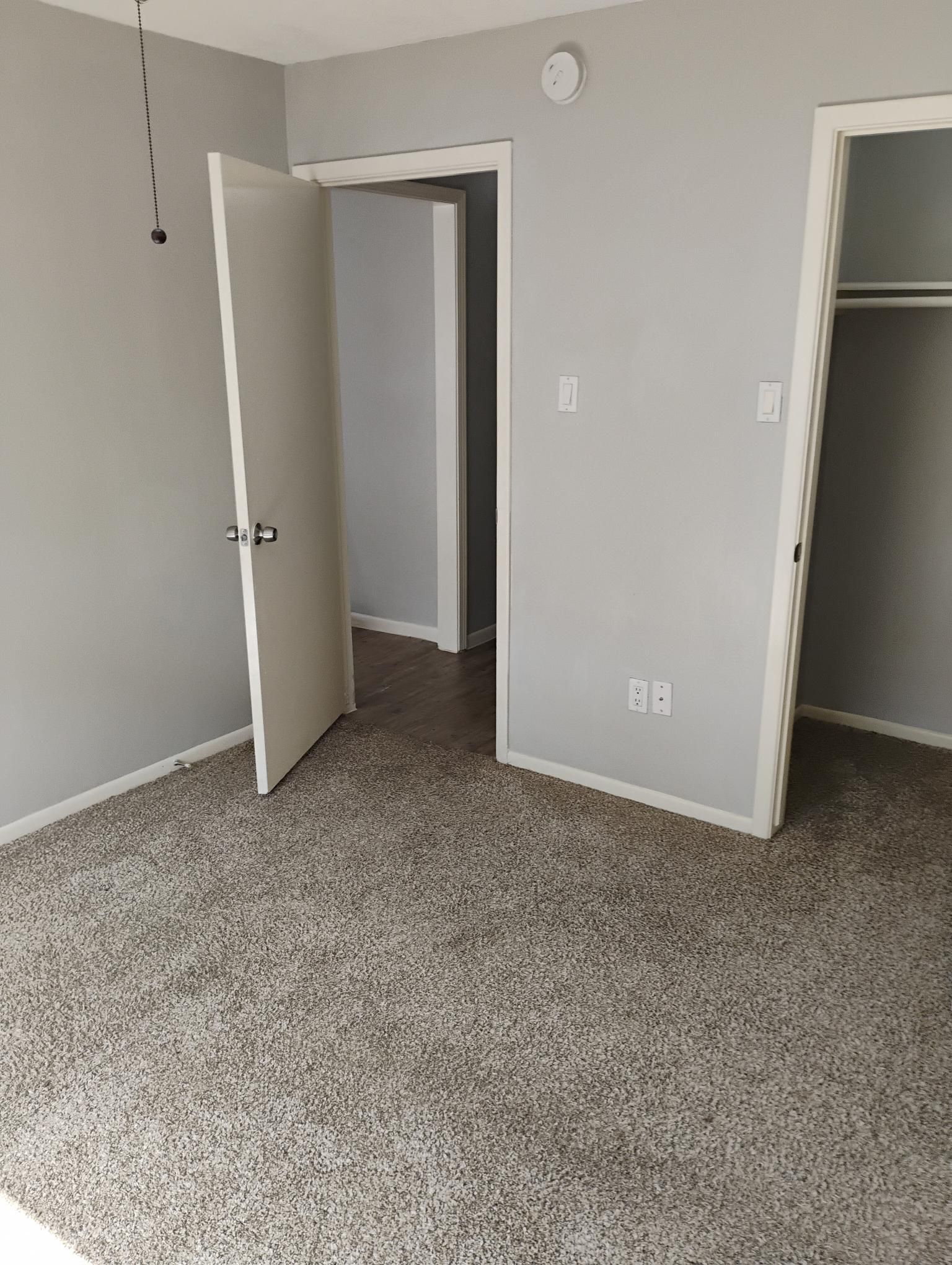 Empty bedroom with gray walls, neutral carpet, and three doorways.