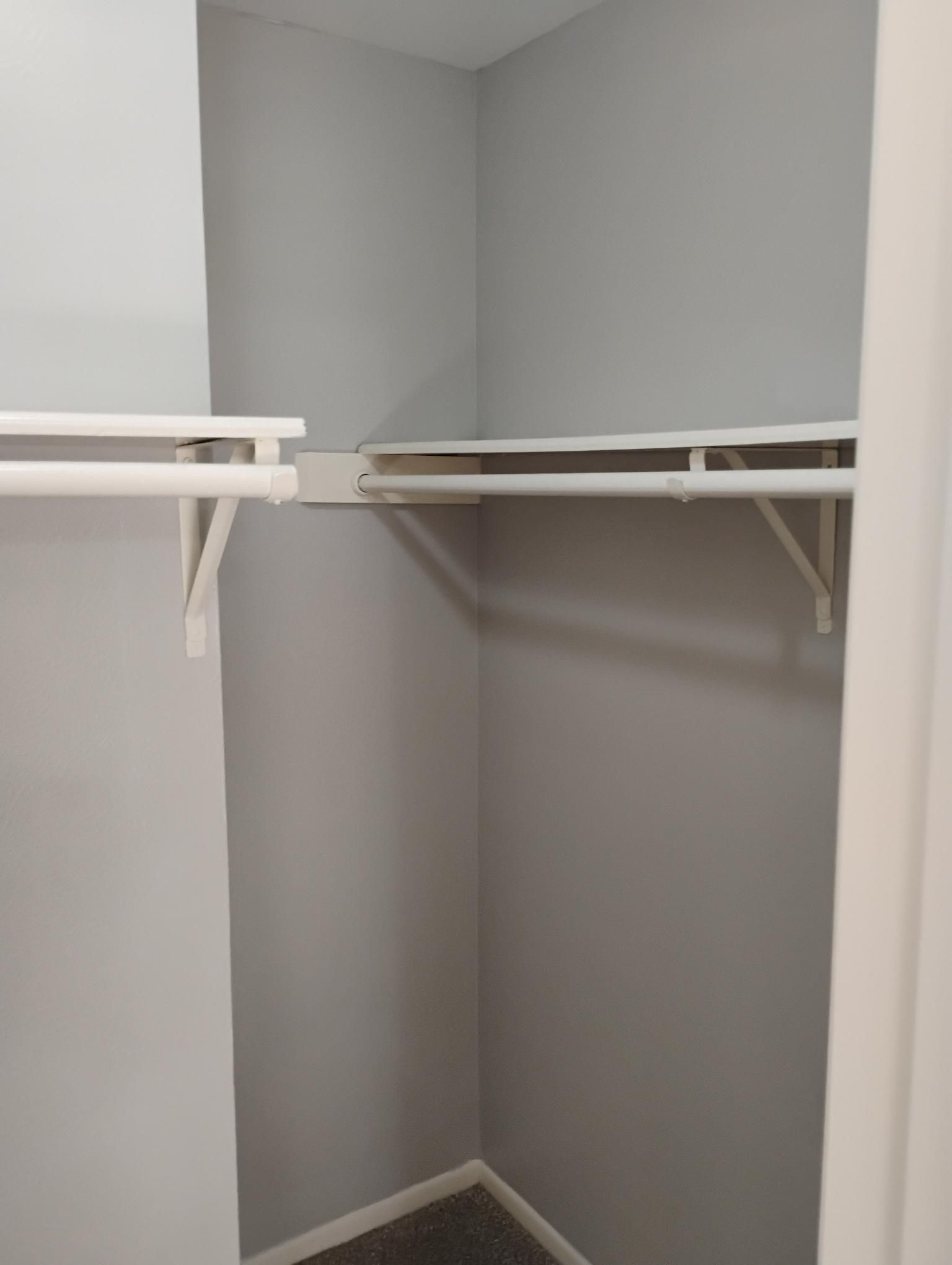 Empty gray closet with two white shelves and a white clothes rod.