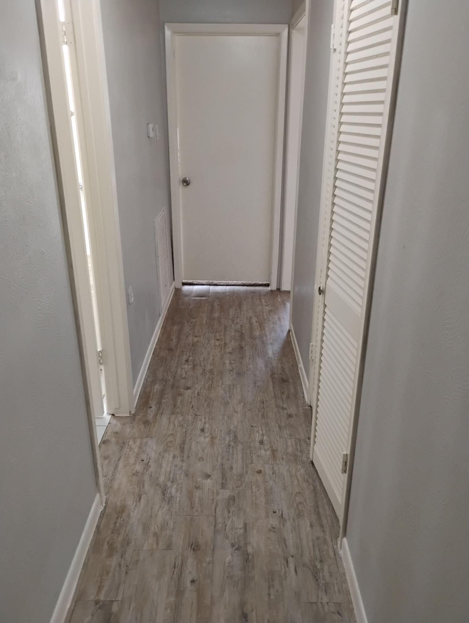 Narrow hallway with gray walls, light wood-look floor, and a closed white door at the end.