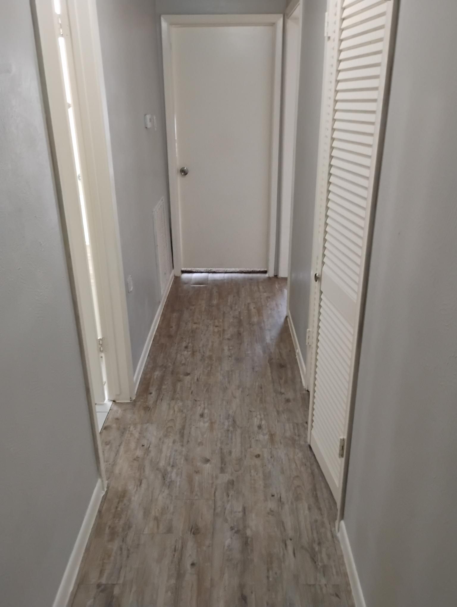 Narrow hallway with gray walls, wood-look floor, and white doors.