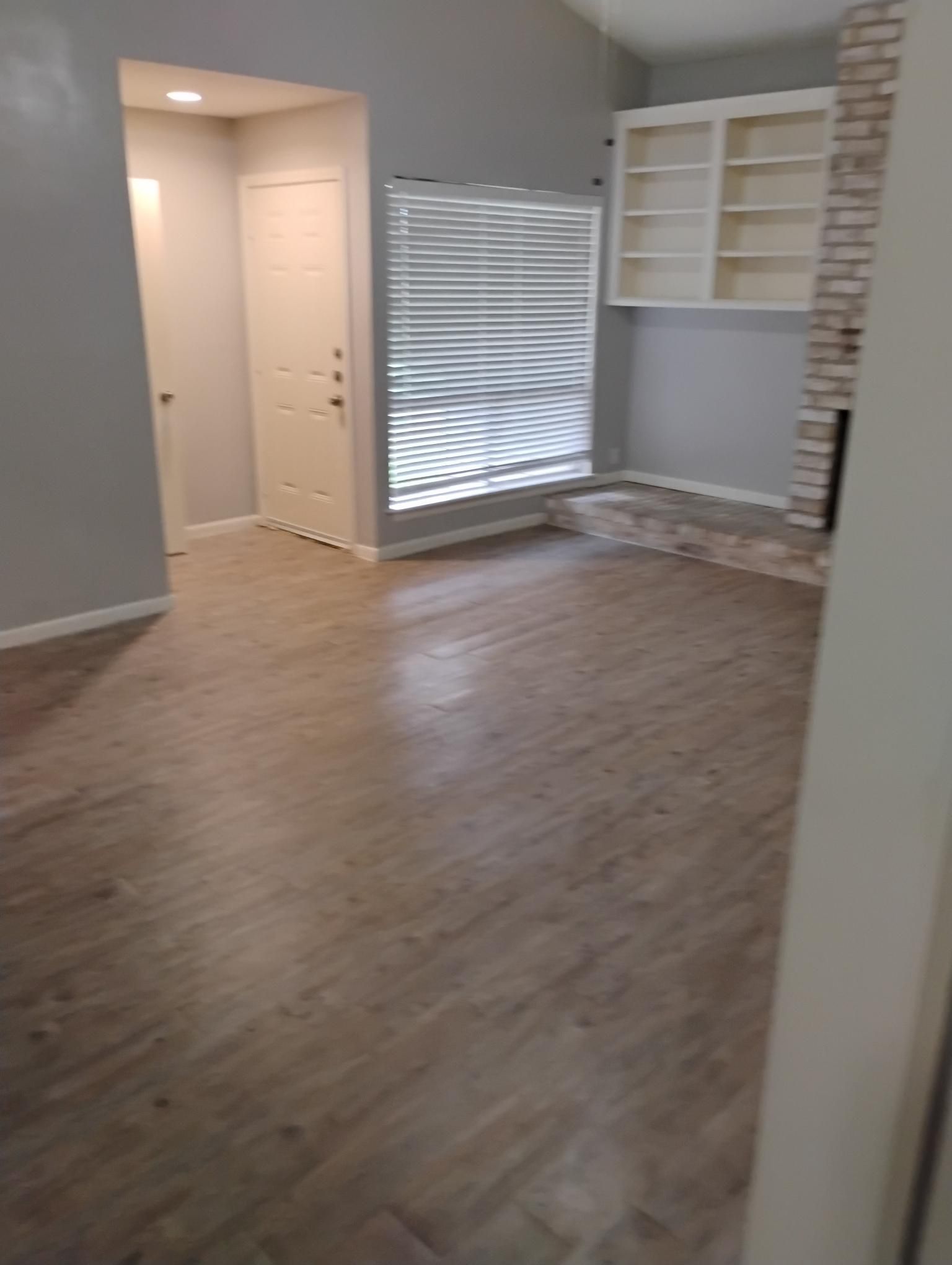Interior view of a living room with gray walls, wood-look flooring, a window, and a built-in bookshelf.