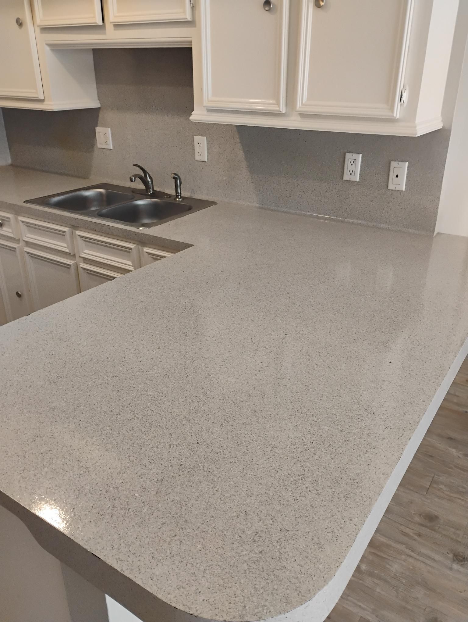 Gray speckled countertop and backsplash in kitchen with white cabinets and a double sink.