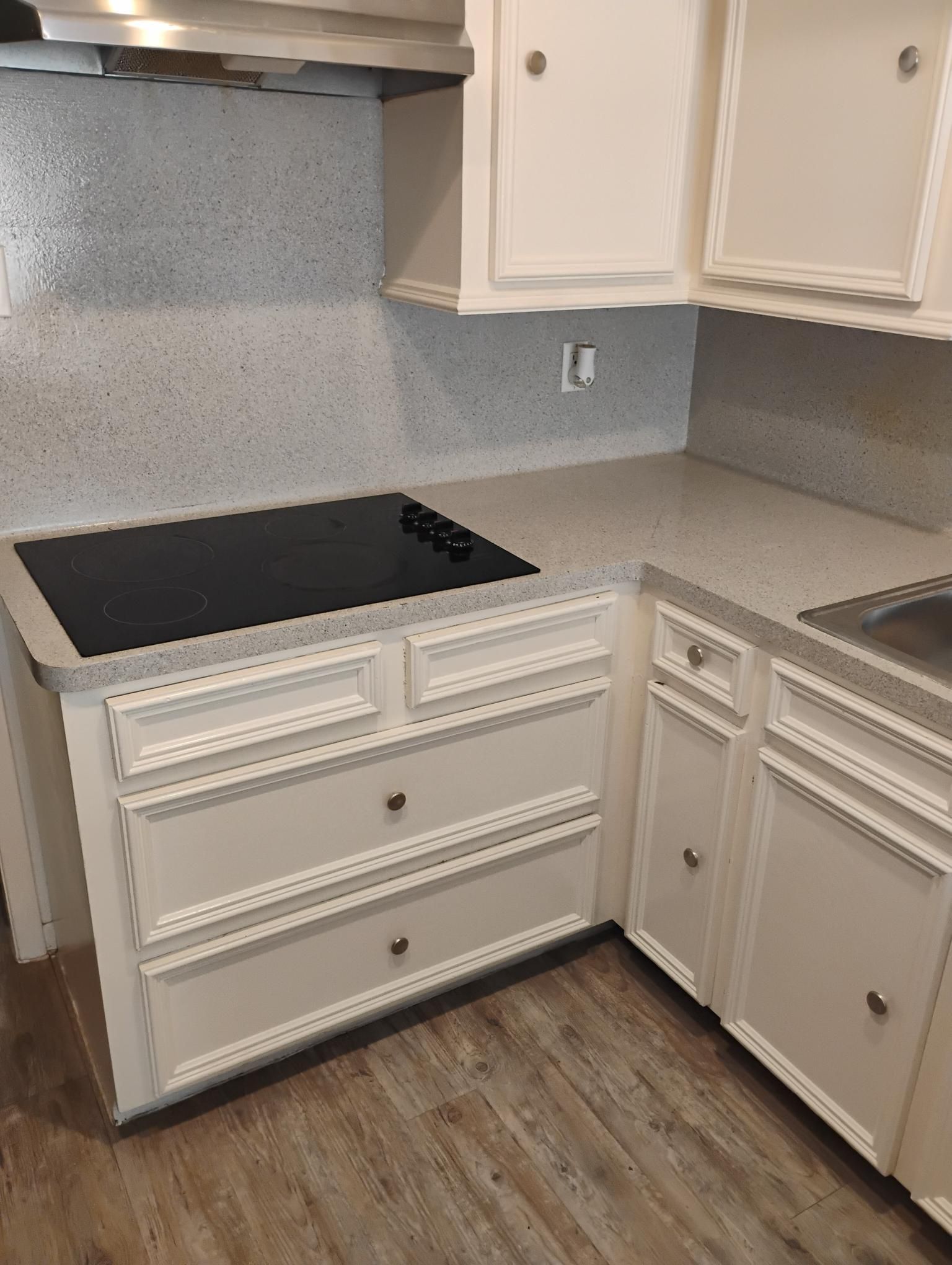 Kitchen corner with white cabinets, gray countertop, and black stovetop.