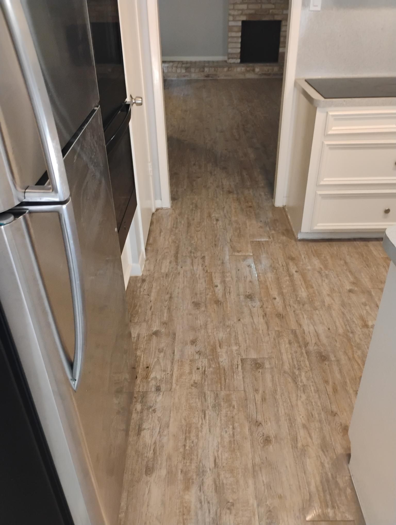 Kitchen with light brown flooring, stainless steel fridge, and doorway leading to a room with a fireplace.